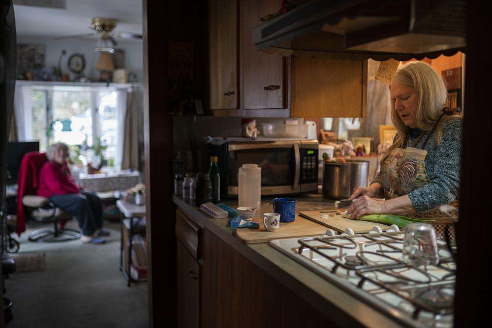 Nancy Rose, right, who contracted COVID-19 in 2021 and continues to exhibit long-haul symptoms including brain fog and memory difficulties, cooks for her mother, Amy Russell, left, at their home, on Tuesday, in Port Jefferson, N.Y.