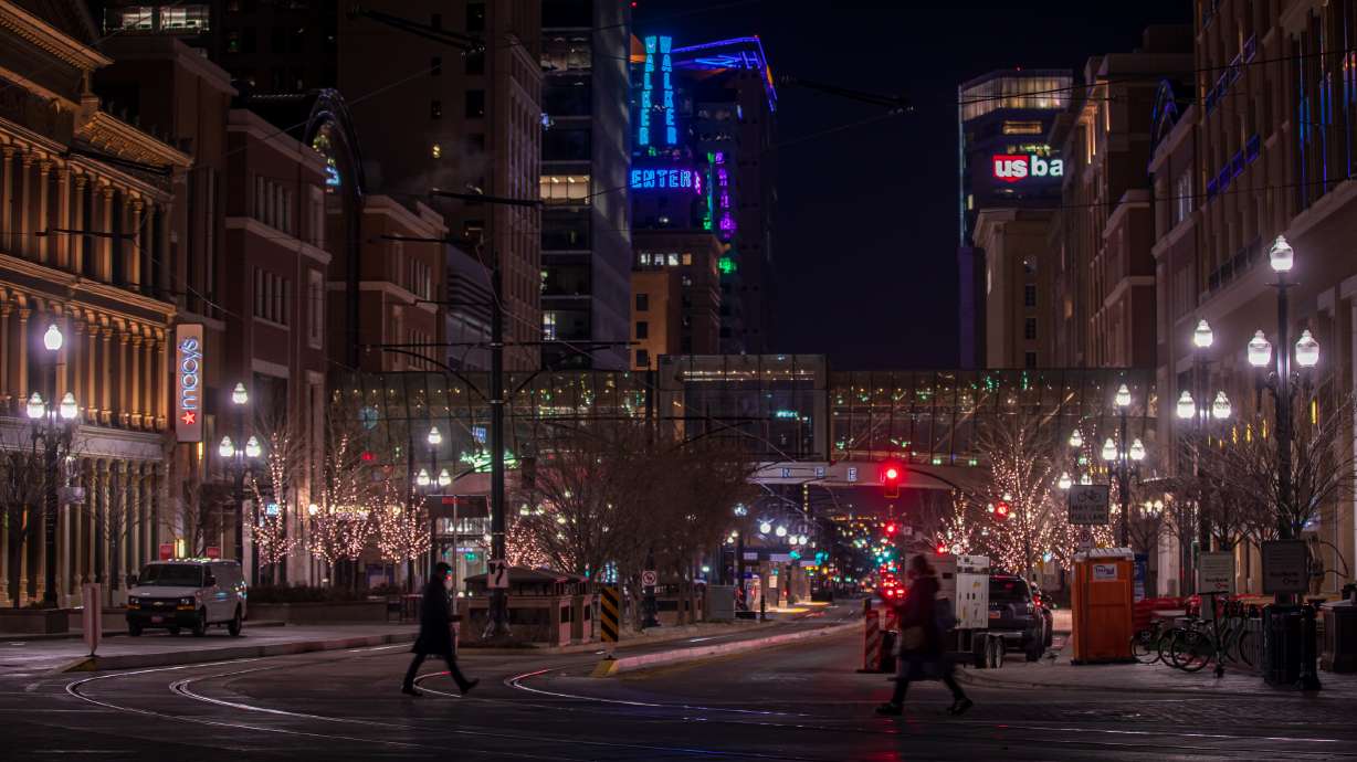 People walk through downtown Salt Lake City on Thursday night, with the Walker Center tower lit up in the background. Crews recently replaced the old neon lighting strips with LED strips.