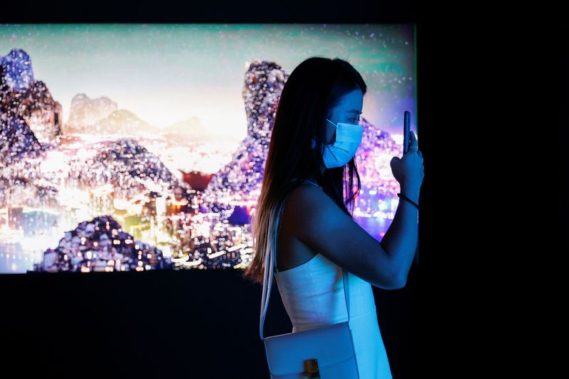 A visitor takes a photo in front of a video installation "Glows in the Night" by Chinese contemporary artist Yang Yongliang, which will be converted into NFTs and auctioned online at Sotheby's, at the Digital Art Fair, in Hong Kong. 