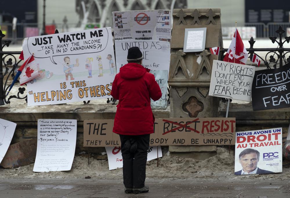 A woman stops to take a photo of signs attached to the fence around Parliament as a trucker protest continues, Wednesday in Ottawa, Canada.