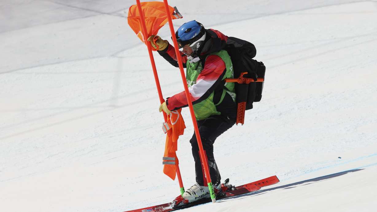 A course worker removes a flag from a gate on the men's downhill course after race was postponed due to high winds at the 2022 Winter Olympics, Sunday, Feb. 6, 2022, in the Yanqing district of Beijing.
