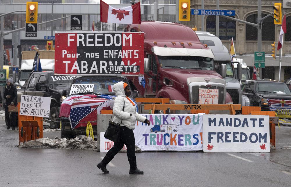 A woman crosses the street in front of vehicles parked as part of the trucker protest, Tuesday, in Ottawa.