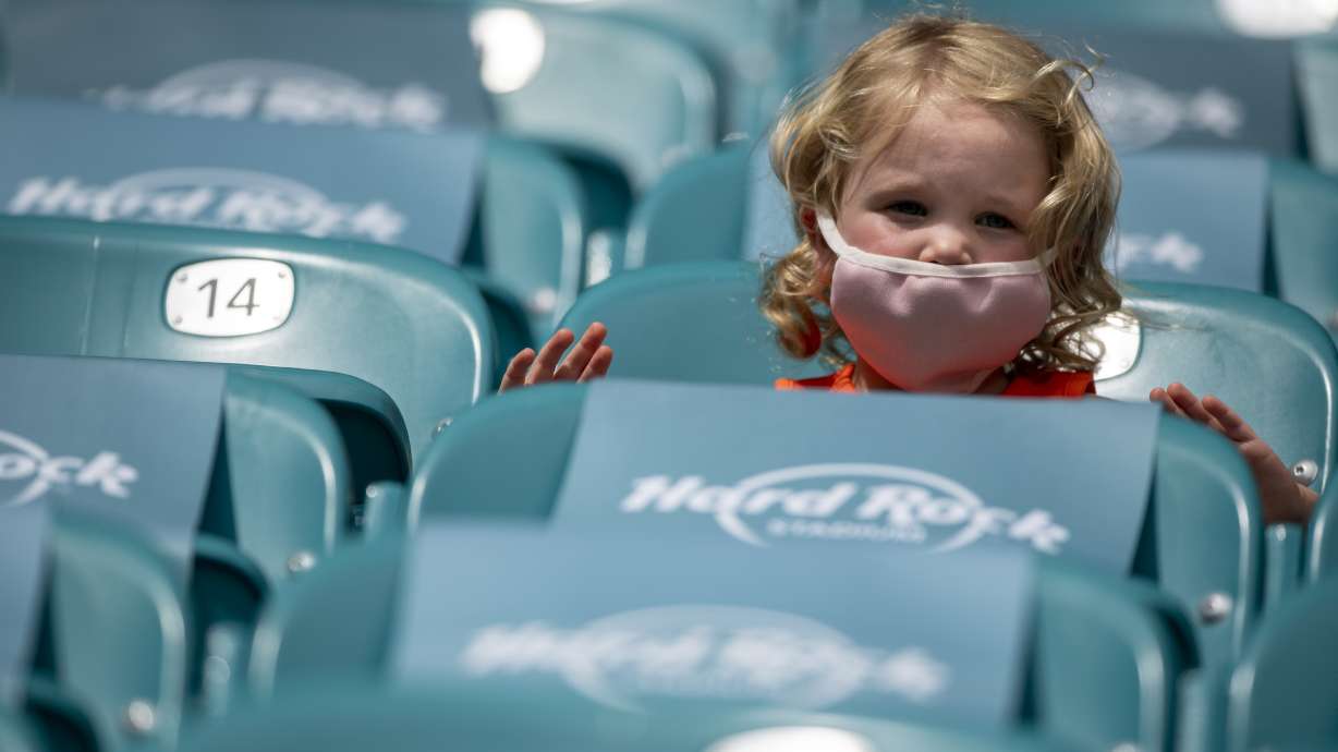 A young child wears a mask in the socially distance seating at the Hard Rock Stadium before the Seattle Seahawks take on the Miami Dolphins during an NFL football game, Oct. 4, 2020, in Miami Gardens, Fla.