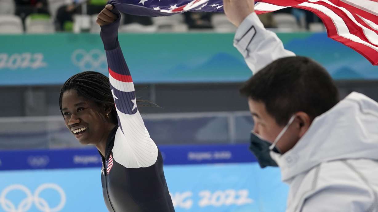 Erin Jackson of the United States holds up an American flag with coach Ryan Shimabukuro after winning the gold medal in the speedskating women's 500-meter race at the 2022 Winter Olympics, Sunday, Feb. 13, 2022, in Beijing.