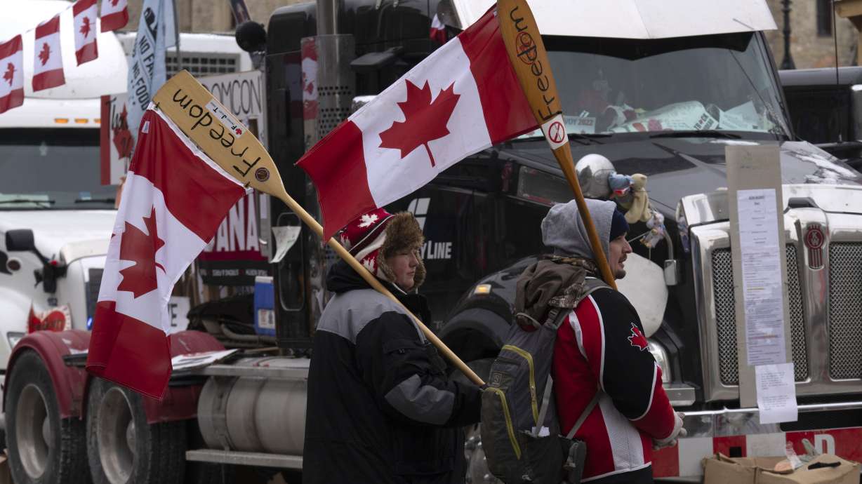 Surrounded by trucks, two protesters carry canoe paddles as flagpoles, Wednesday in Ottawa. Trucks in Canada have been clogging crossings at the U.S. border for more than two weeks.