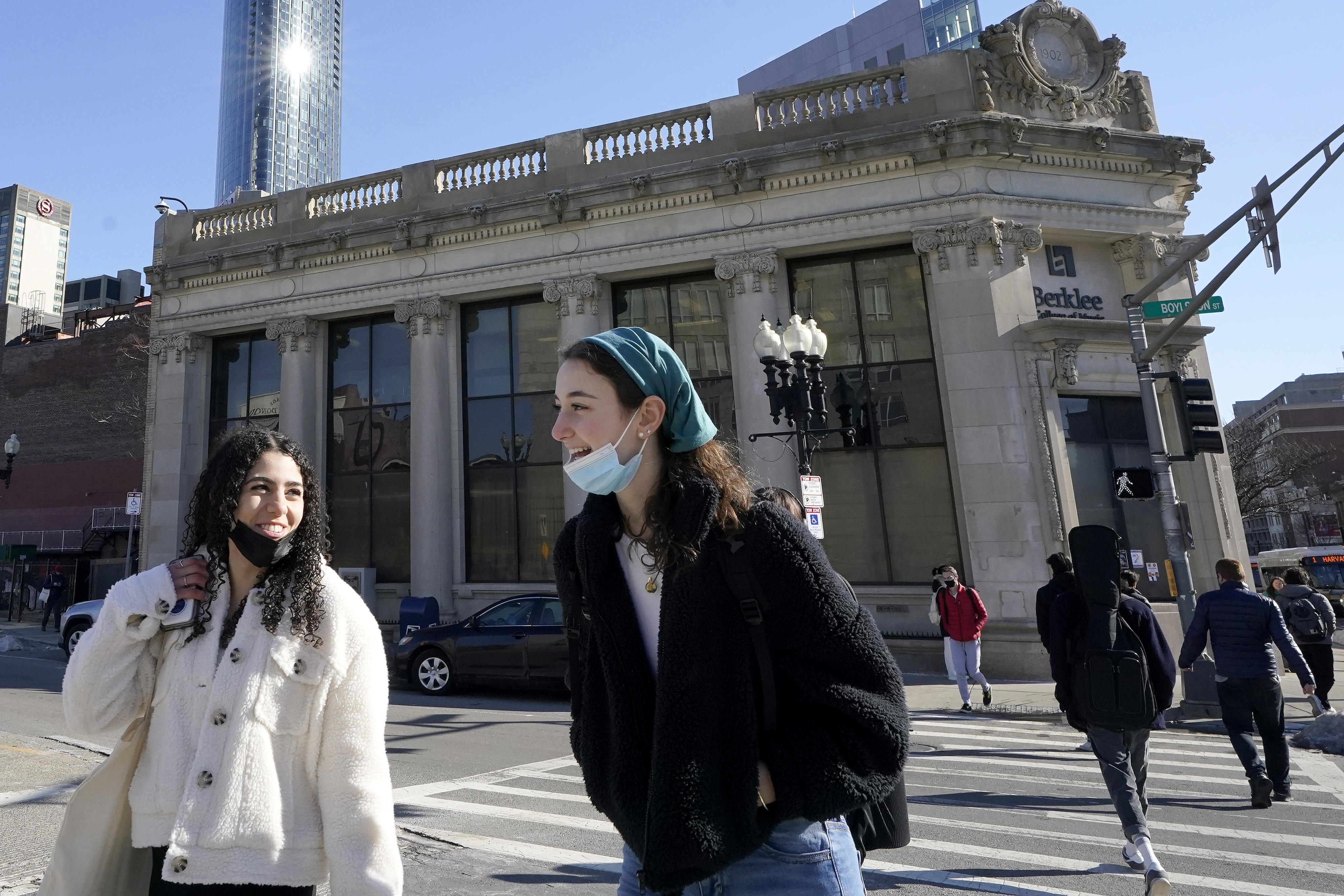 Passers-by wear masks under their chins as they chat with one another while crossing a street, in Boston, Wednesday, Feb. 9. Students and staff at public schools in Massachusetts will no longer be required to wear face coverings while indoors starting Feb. 28, state officials said.