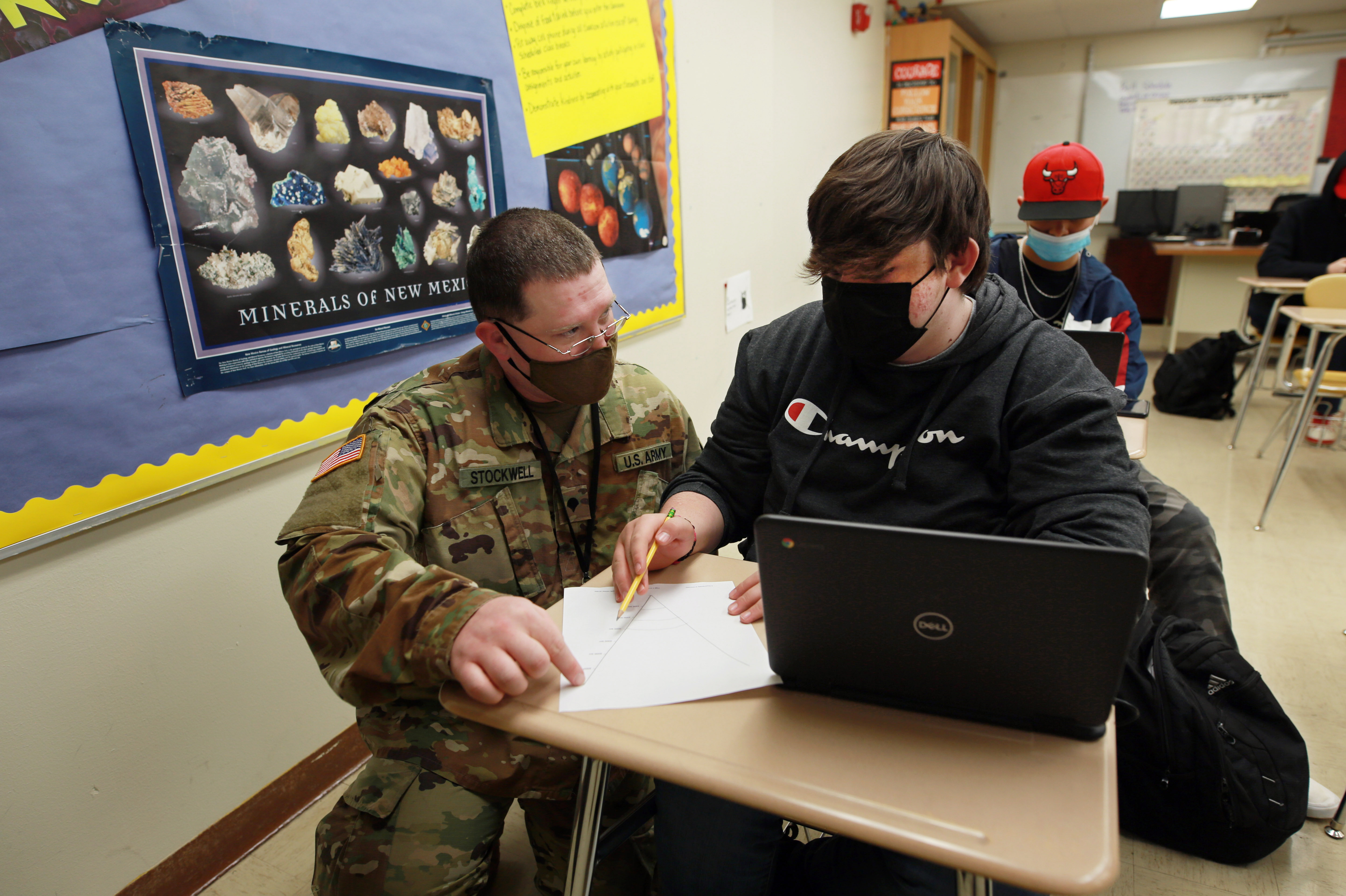New Mexico Army National Guard specialist Michael Stockwell kneels while helping Alamogordo High School freshman Aiden Cruz with a geology assignment, at Alamogordo High School, Tuesday, Feb. 8, in Alamogordo, N.M. Dozens of National Guard Army and Air Force troops in New Mexico have been stepping in for the shortage of teachers and school staff.