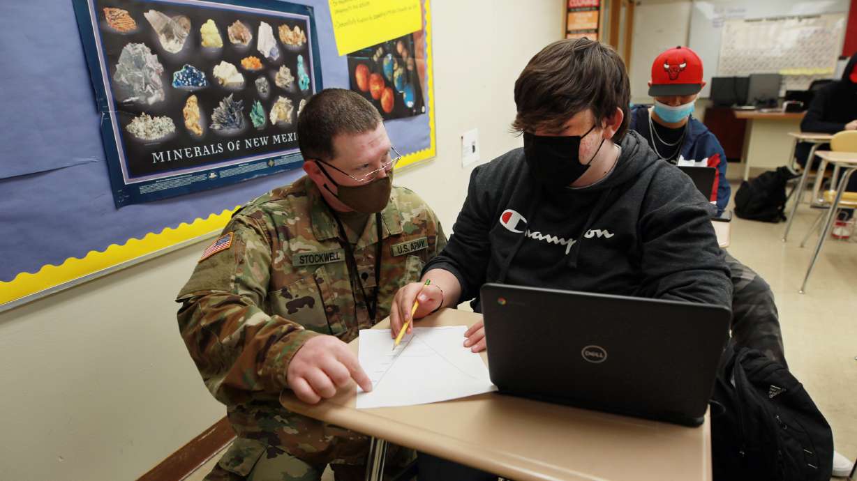 New Mexico Army National Guard specialist Michael Stockwell kneels while helping Alamogordo High School freshman Aiden Cruz with a geology assignment, at Alamogordo High School, Tuesday, Feb. 8, in Alamogordo, N.M. Dozens of National Guard Army and Air Force troops in New Mexico have been stepping in for the shortage of teachers and school staff.