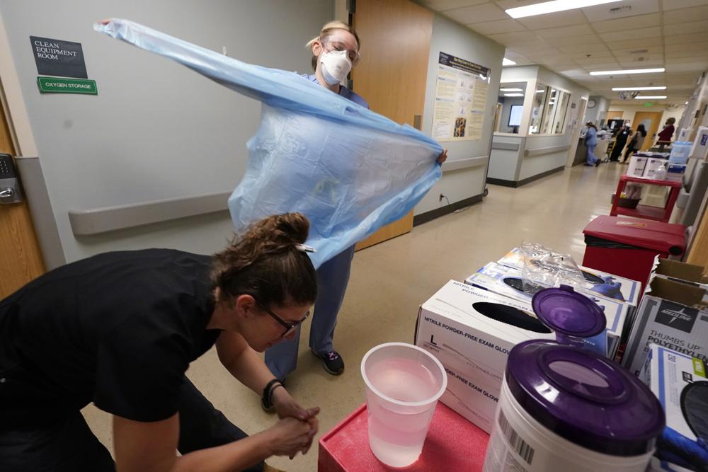 Registered nurse Jessalynn Dest, left, removes protective equipment and washes her hands after leaving a COVID-19 patient's room as speech therapist Sam Gibbs puts on safety clothing while preparing to see a patient in the acute care unit of Harborview Medical Center, Friday in Seattle. Tens of millions of people remain vulnerable to COVID-19.