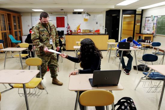 Substitute teacher and New Mexico Army National Guard specialist Michael Stockwell takes a geology assignment from Lilli Terrazas, 15, at Alamogordo High School, Tuesday, Feb. 8, 2022, in Alamogordo, N.M.