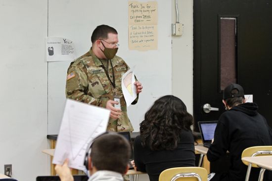 Substitute teacher and New Mexico Army National Guard specialist Michael Stockwell substitute holds up a geology assignment while teaching students at Alamogordo High School, Tuesday, Feb. 8, 2022, in Alamogordo, N.M. National Guard units are assisting in schools in the face of staff shortages.