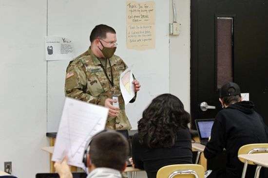 Substitute teacher and New Mexico Army National Guard specialist Michael Stockwell substitute holds up a geology assignment while teaching students at Alamogordo High School, Tuesday, Feb. 8, 2022, in Alamogordo, N.M. National Guard units are assisting in schools in the face of staff shortages.