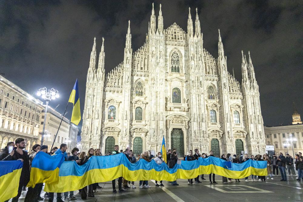 People hold a large flag of Ukraine in Duomo Square, Milan, Italy, Thursday. Russian President Vladimir Putin on Thursday announced a military operation in Ukraine and warned other countries that any attempt to interfere with the Russian action would lead to 'consequences you have never seen.'