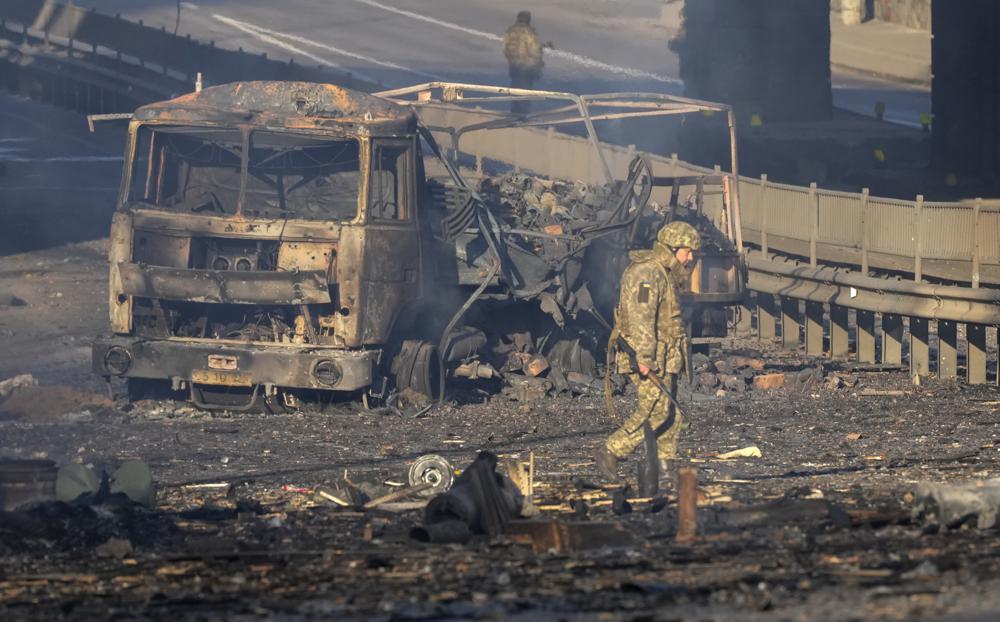 A Ukrainian soldier walks past debris of a burning military truck, on a street in Kyiv, Ukraine, Saturday. The United States, European Union and the United Kingdom on Saturday agreed to put in place crippling sanctions on the Russian financial sector.