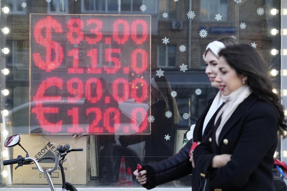 People walk past a currency exchange office screen displaying the exchange rates of U.S. Dollar and Euro to Russian Rubles in Moscow's downtown, Russia, Monday. Ordinary Russians are facing the prospect of higher prices as Western sanctions over the invasion of Ukraine sent the ruble plummeting.