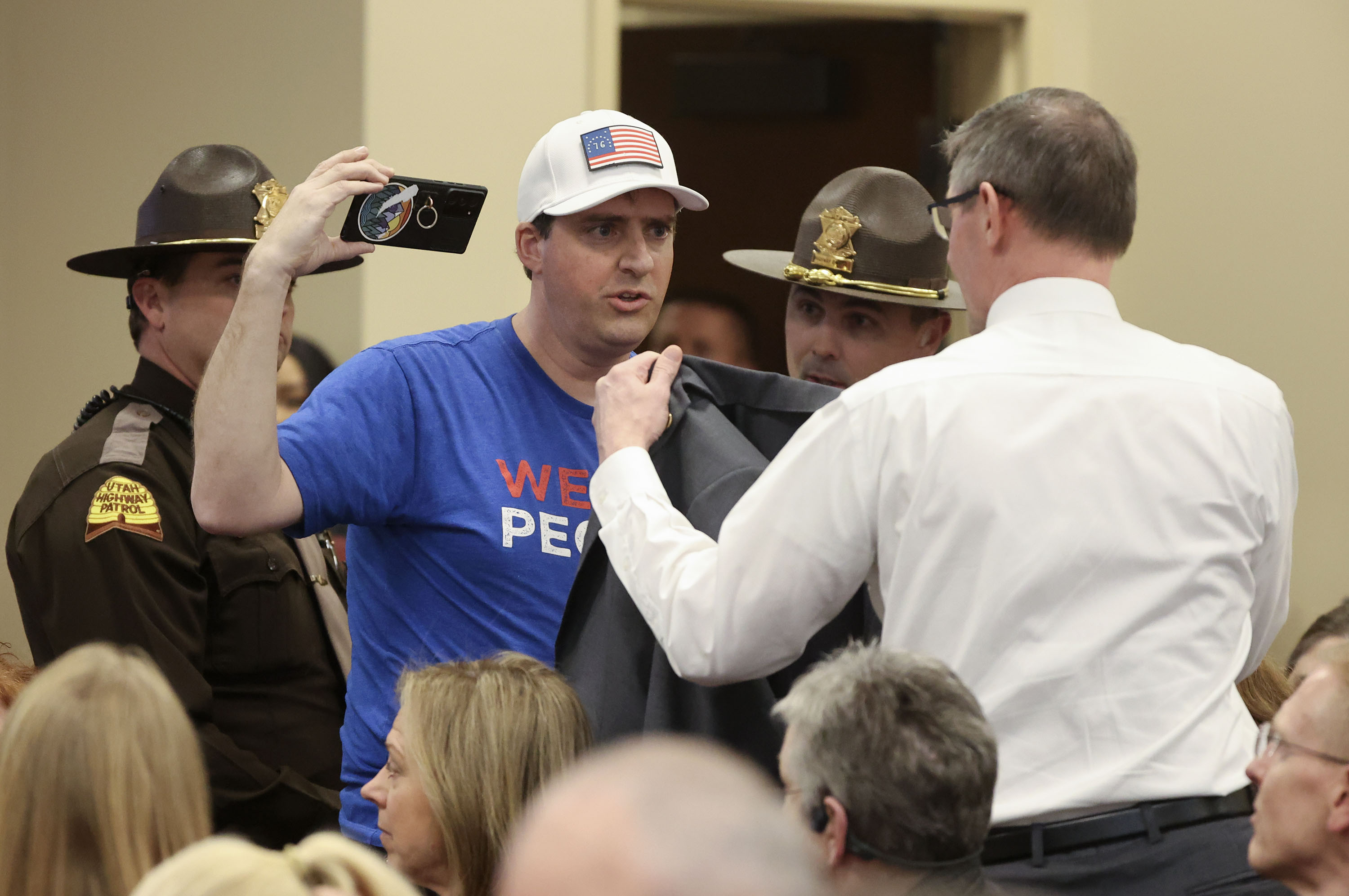 Sen. Mike Kennedy, R-Alpine, offers his coat to a man as Utah Highway Patrol troopers ask the man to leave for violating committee meeting rules by failing to cover up a political shirt, before the start of discussion on HB60S02 vaccine passport amendments during a Senate Revenue and Taxation Standing Committee meeting in the Senate building in Salt Lake City on Tuesday. The man declined Kennedy’s offer. The man was also previously displaying political stickers, but did put the stickers away when asked.