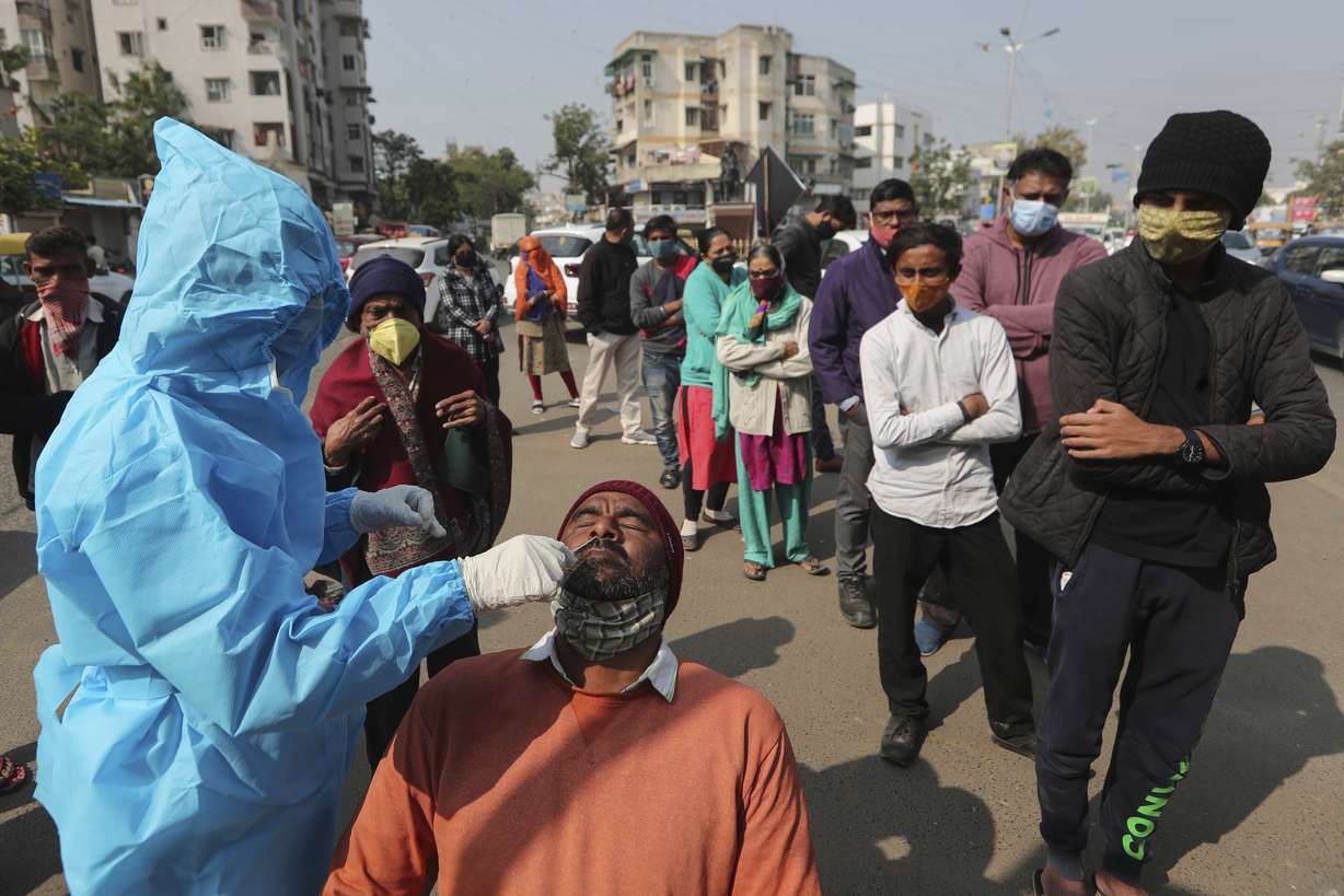 A health worker takes a swab sample of a man to test for the coronavirus as others wait to get tested in Ahmedabad, India, Monday, Jan. 17, 2022. The official global death toll from COVID-19 is on the verge of eclipsing 6 million — underscoring that the pandemic, now in its third year, is far from over.