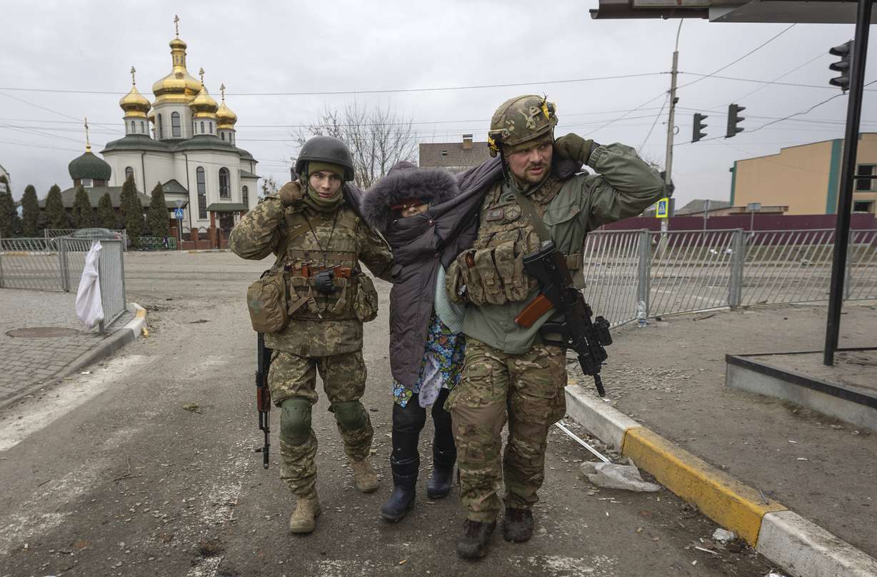 Ukrainian servicemen help an elderly woman, in the town of Irpin, Ukraine, Sunday. With the Kremlin's rhetoric growing fiercer and a reprieve from fighting dissolving, Russian troops continued to shell encircled cities and the number of Ukrainians forced from their country grew to over 1.4 million.