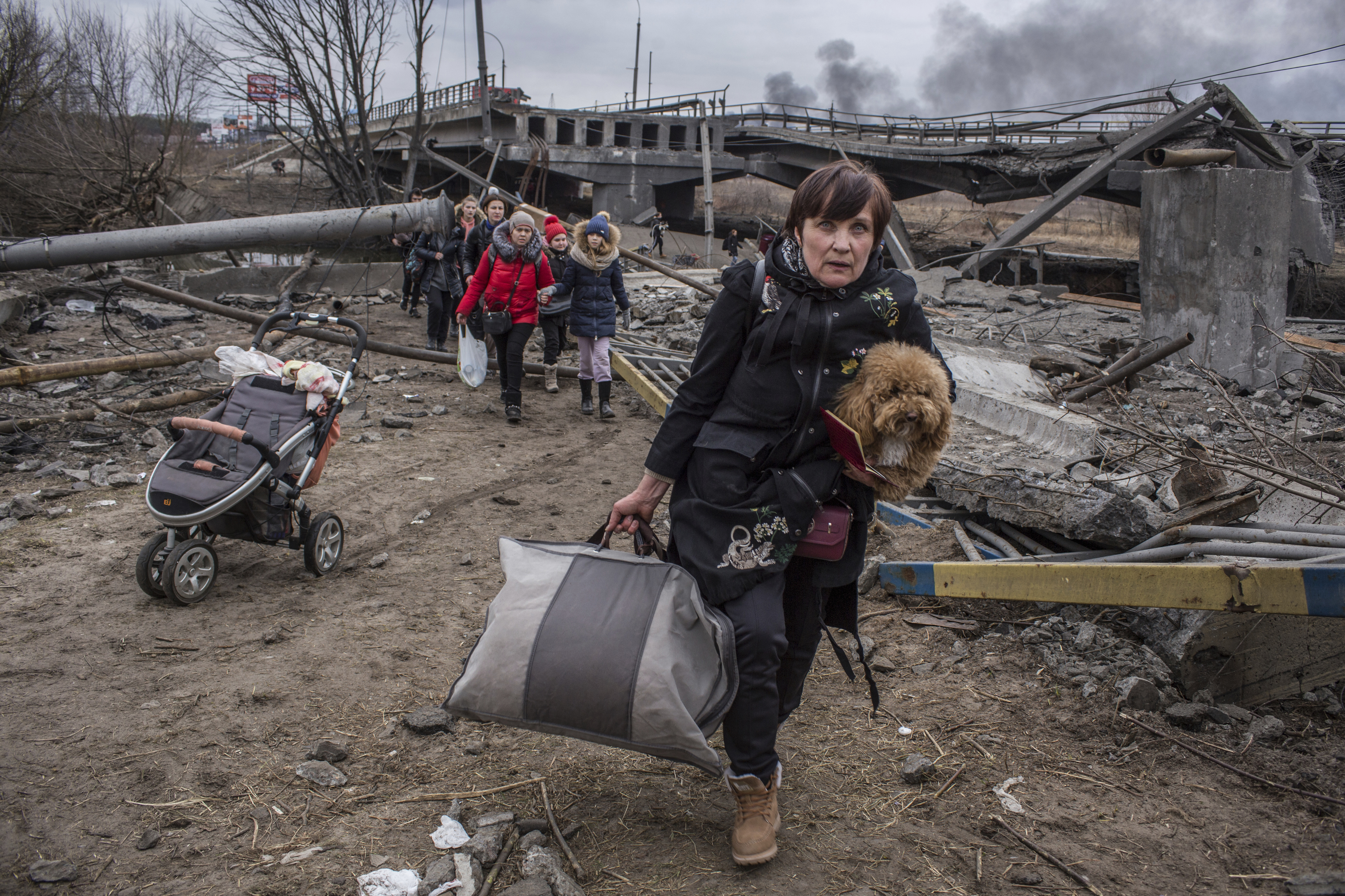 People cross an improvised path under a destroyed bridge while fleeing the town of Irpin, Ukraine, Sunday, March 6, 2022. In Irpin, near Kyiv, a sea of people on foot and even in wheelbarrows trudged over the remains of a destroyed bridge to cross a river and leave the city.
