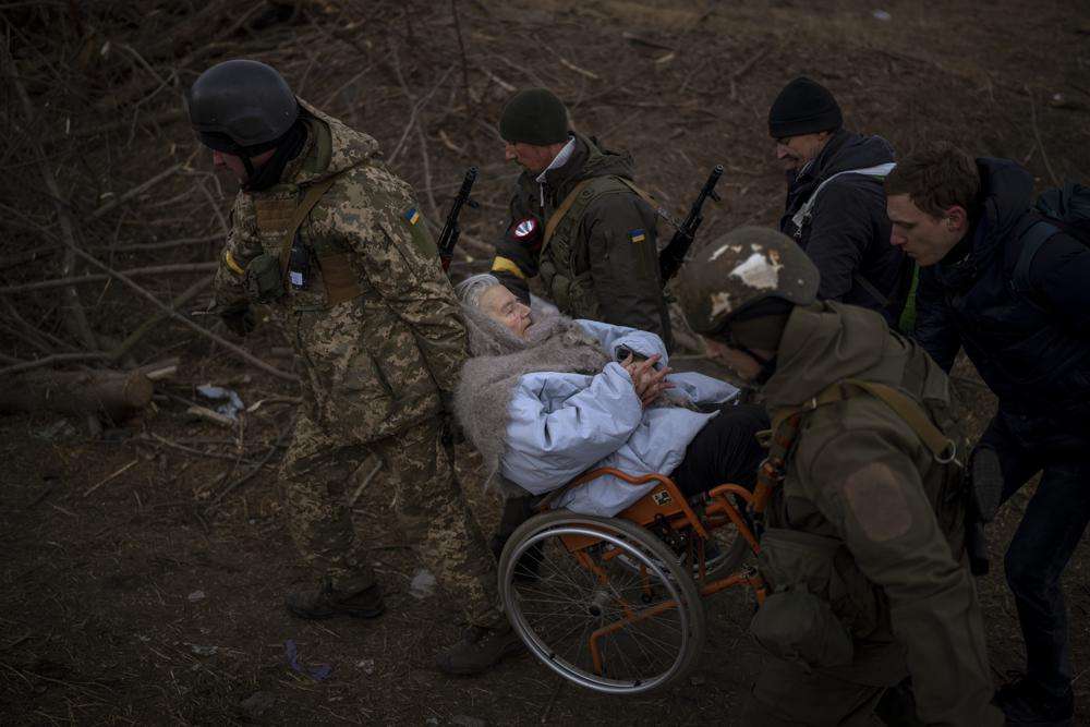 Ukrainian soldiers and militiamen carry a woman in a wheelchair as the artillery echoes nearby, while people flee Irpin on the outskirts of Kyiv, Ukraine, Monday. Russia announced yet another cease-fire and a handful of humanitarian corridors to allow civilians to flee Ukraine. Previous such measures have fallen apart and Moscow's armed forces continued to pummel some Ukrainian cities with rockets Monday.