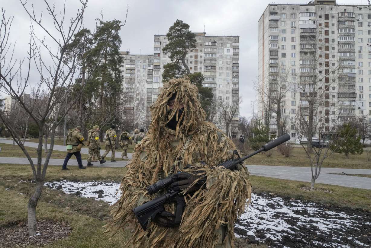Ukrainian Territorial Defence Forces members walk past the city park as a camouflaged soldier stands in foreground, in the outskirts of Kyiv, Ukraine, Wednesday.