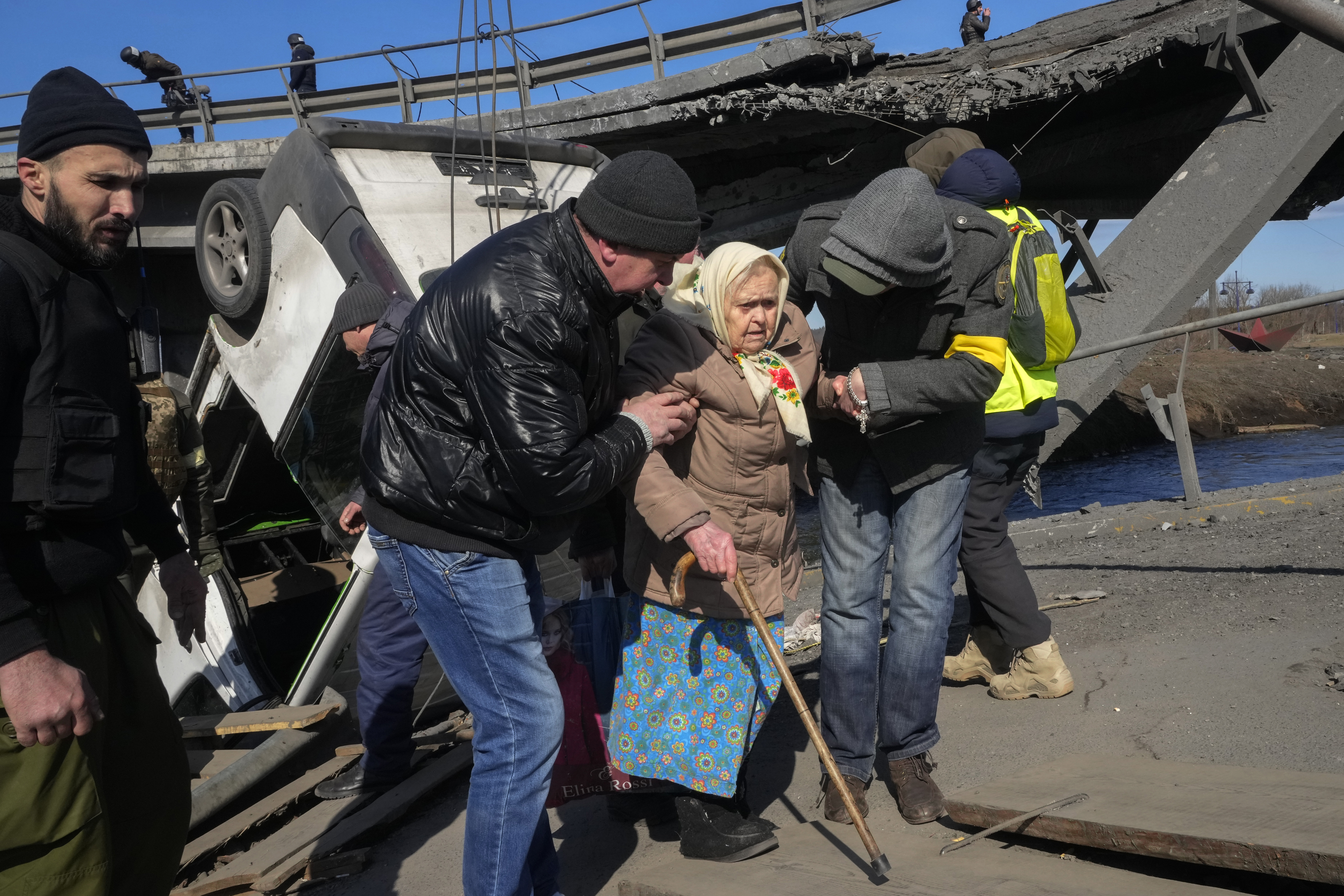 Volunteers pass an improvised path under a destroyed bridge as they evacuate an elderly resident in Irpin, some 16 miles northwest of Kyiv, Friday. Kyiv northwest suburbs such as Irpin and Bucha have been enduring Russian shellfire and bombardments for over a week.