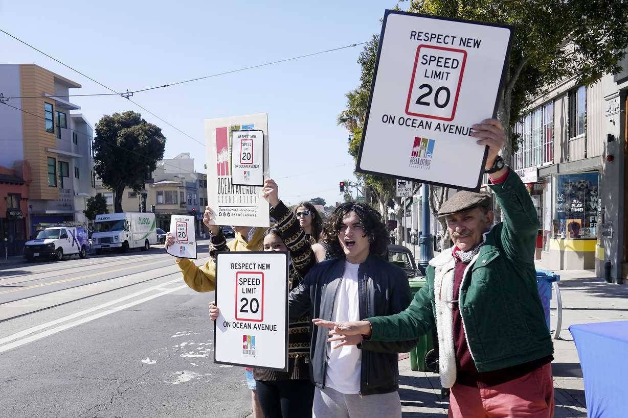 Ocean Avenue Association executive director Pierre Smit, right, and Lick-Wilmerding High School sophomores hold up signs for oncoming traffic at a Slow Down on Ocean Ave event in San Francisco, Wednesday.