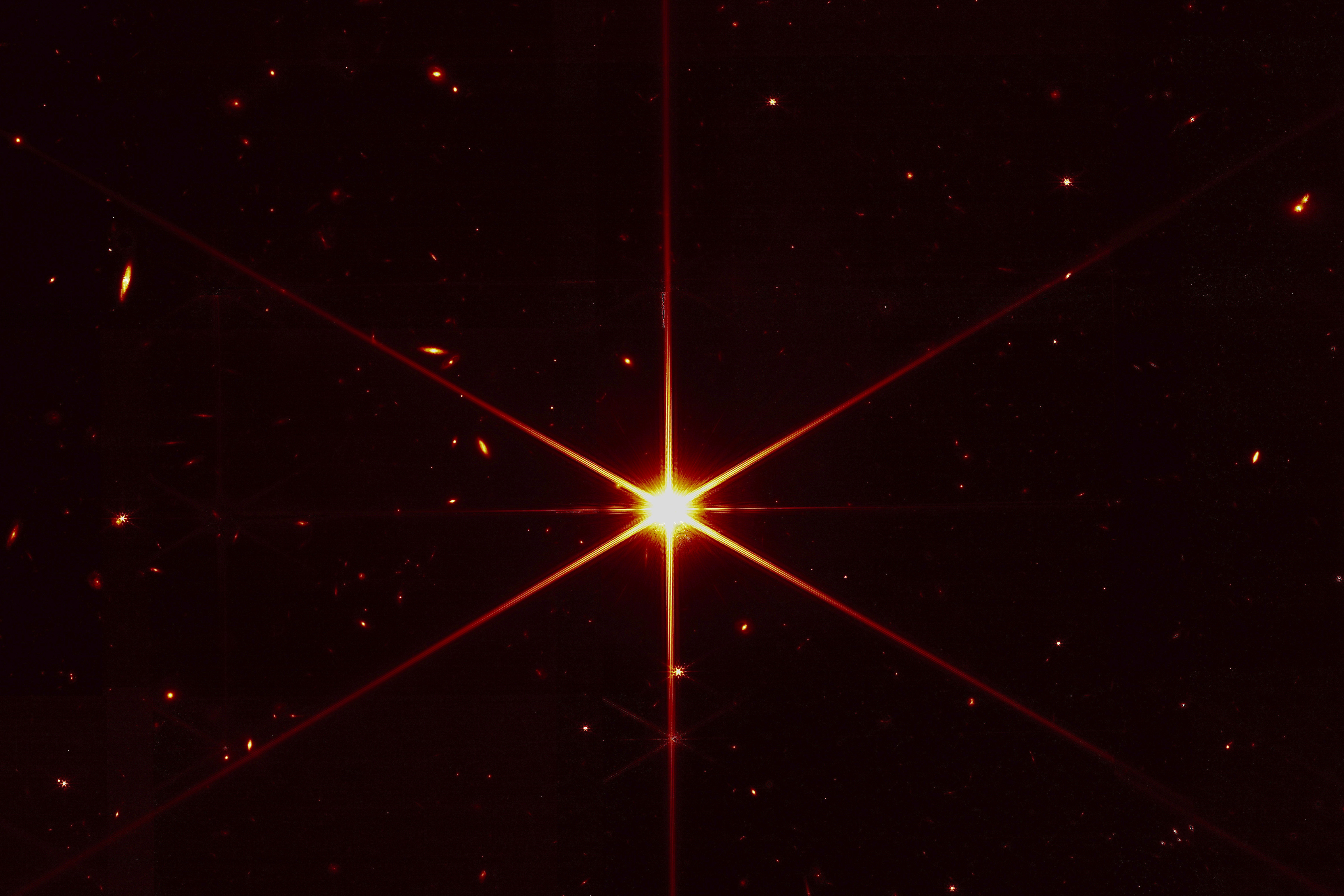 This image made available by NASA on Wednesday shows star 2MASS J17554042+6551277 used to align the mirrors of the James Webb Space Telescope, with galaxies and stars surrounding it. The hexagonal shape of Webb’s mirrors and its filters made the shimmering star look more red and spiky. The first science images aren't expected until late June or early July.