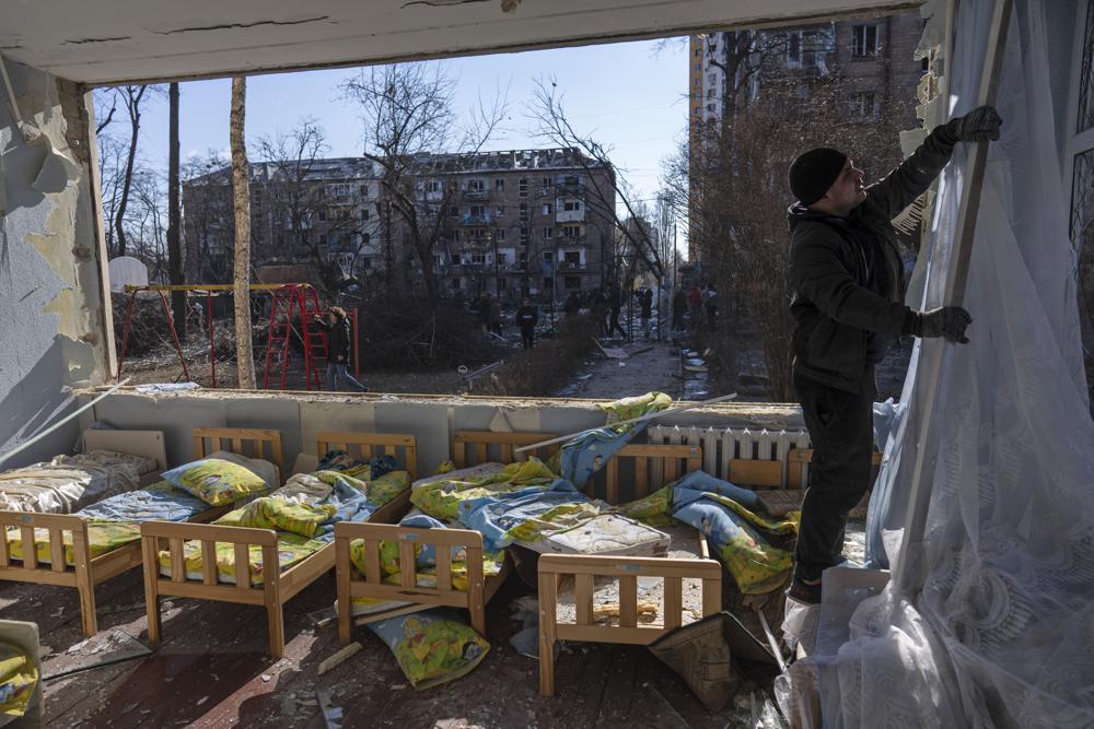 A man removes a destroyed curtain inside a school damaged among other residential buildings in Kyiv, Ukraine, Friday. Russian forces pressed their assault on Ukrainian cities Friday, with new missile strikes and shelling on the edges of the capital Kyiv.