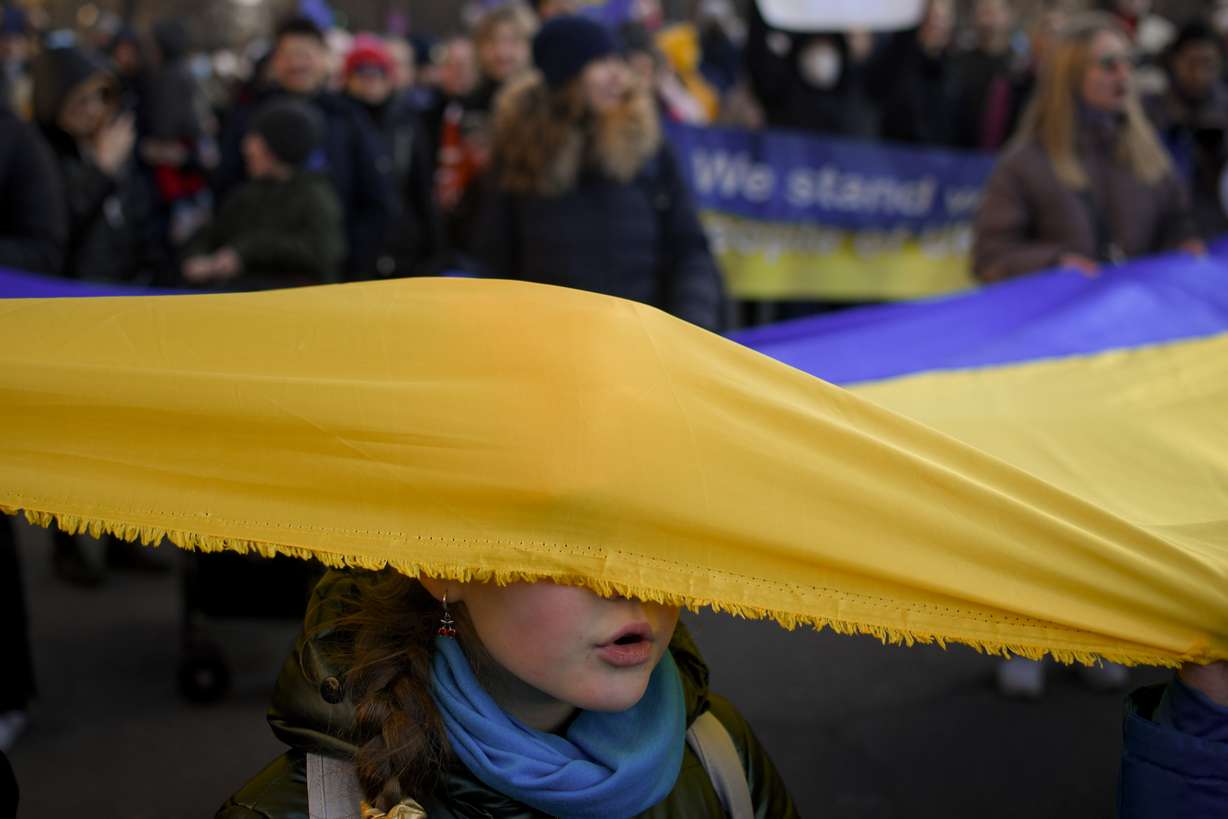 A child with her face covered by a large Ukrainian flag sings the Ukrainian national anthem during a protest against Russia's war in Ukraine, in Bucharest, Romania, Saturday.