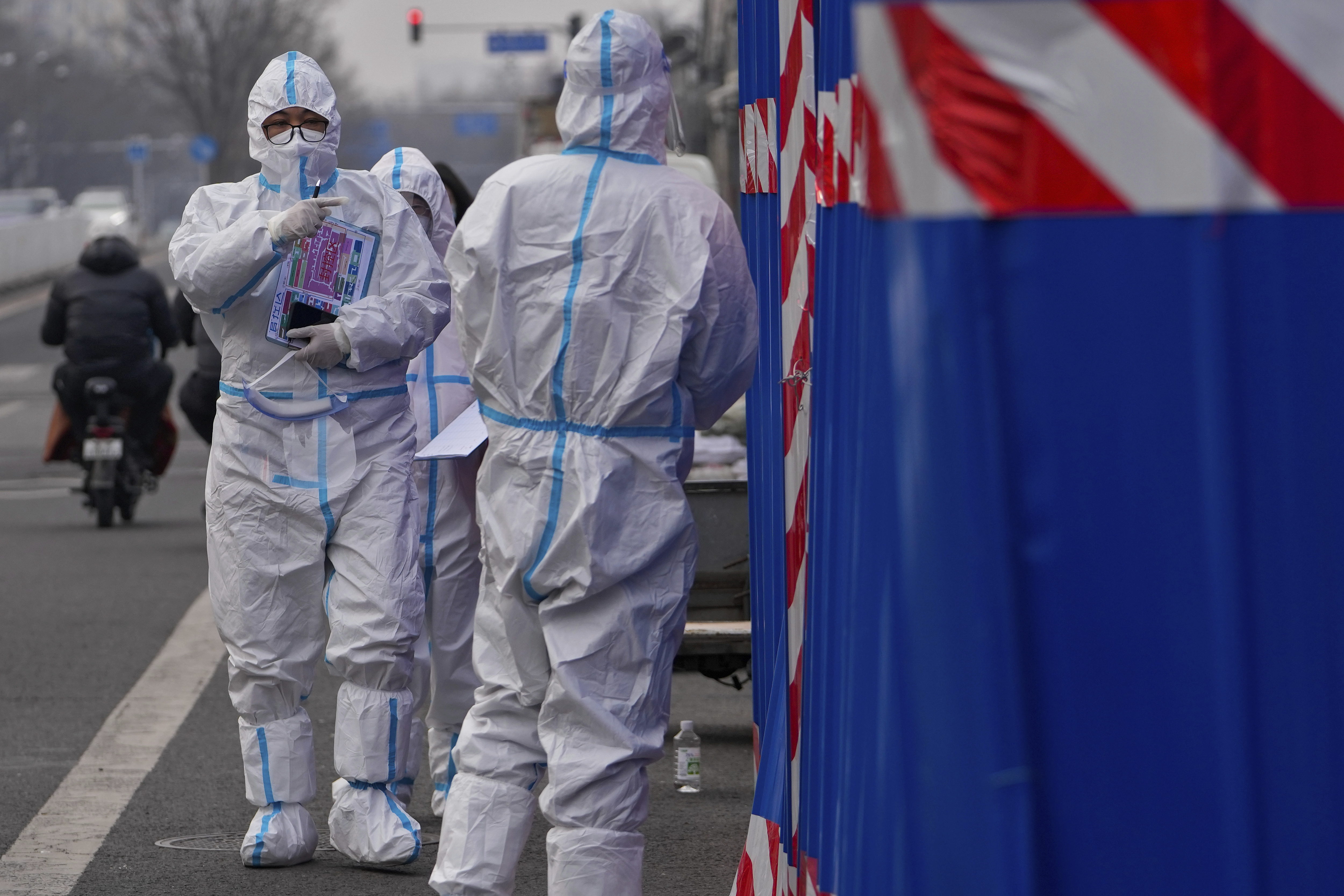 A health worker wearing a protective suit holds a map of sealed control area asks a security guard to open a doorway to a barricaded community that was locked down for health monitoring following the COVID-19 case detected in the area, Wednesday, in Beijing, China.