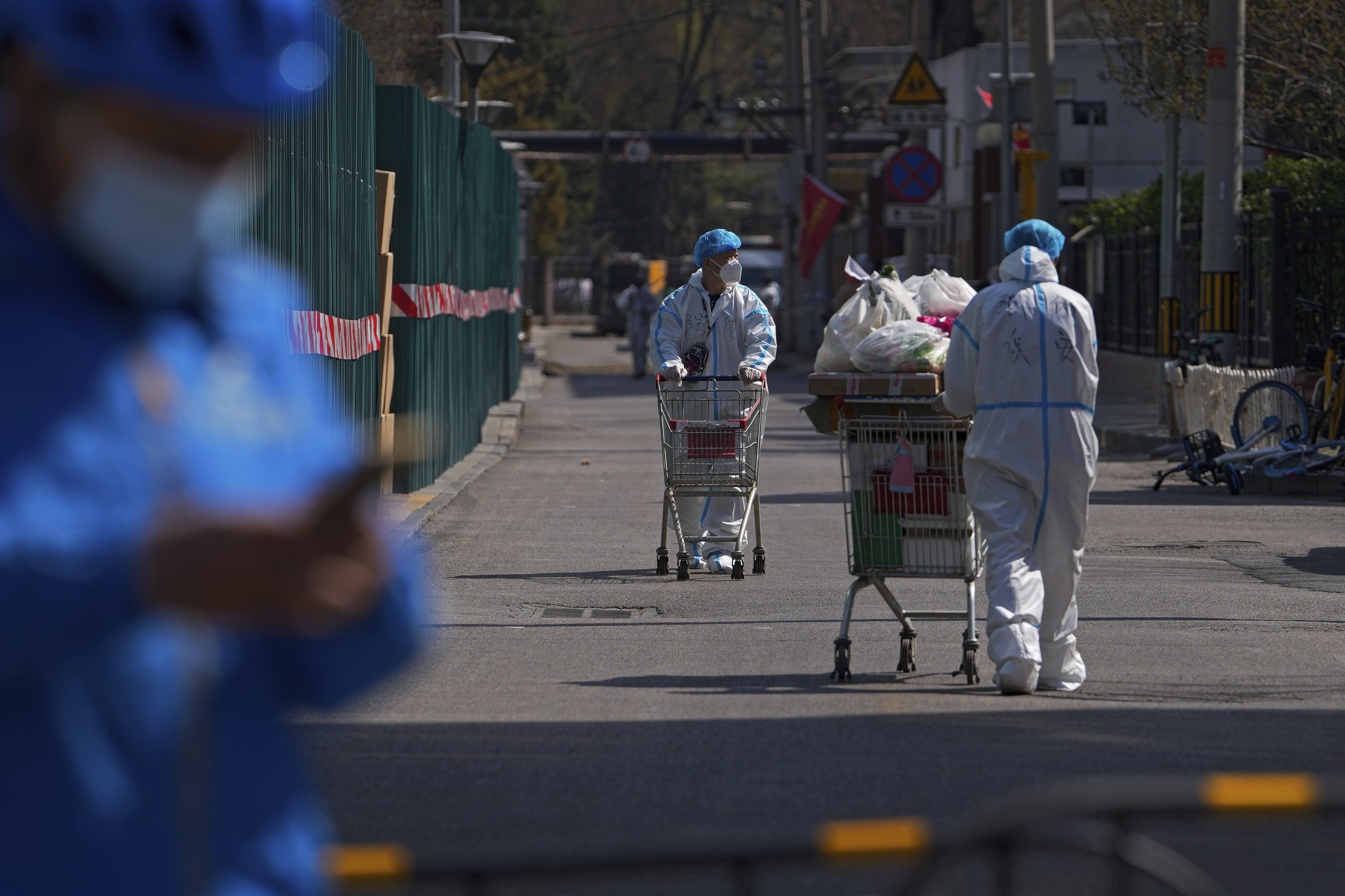 Security guards wearing protective gear transfer goods to barricaded residential buildings locked down for health monitoring following a COVID-19 case detected in the area, Monday, in Beijing.