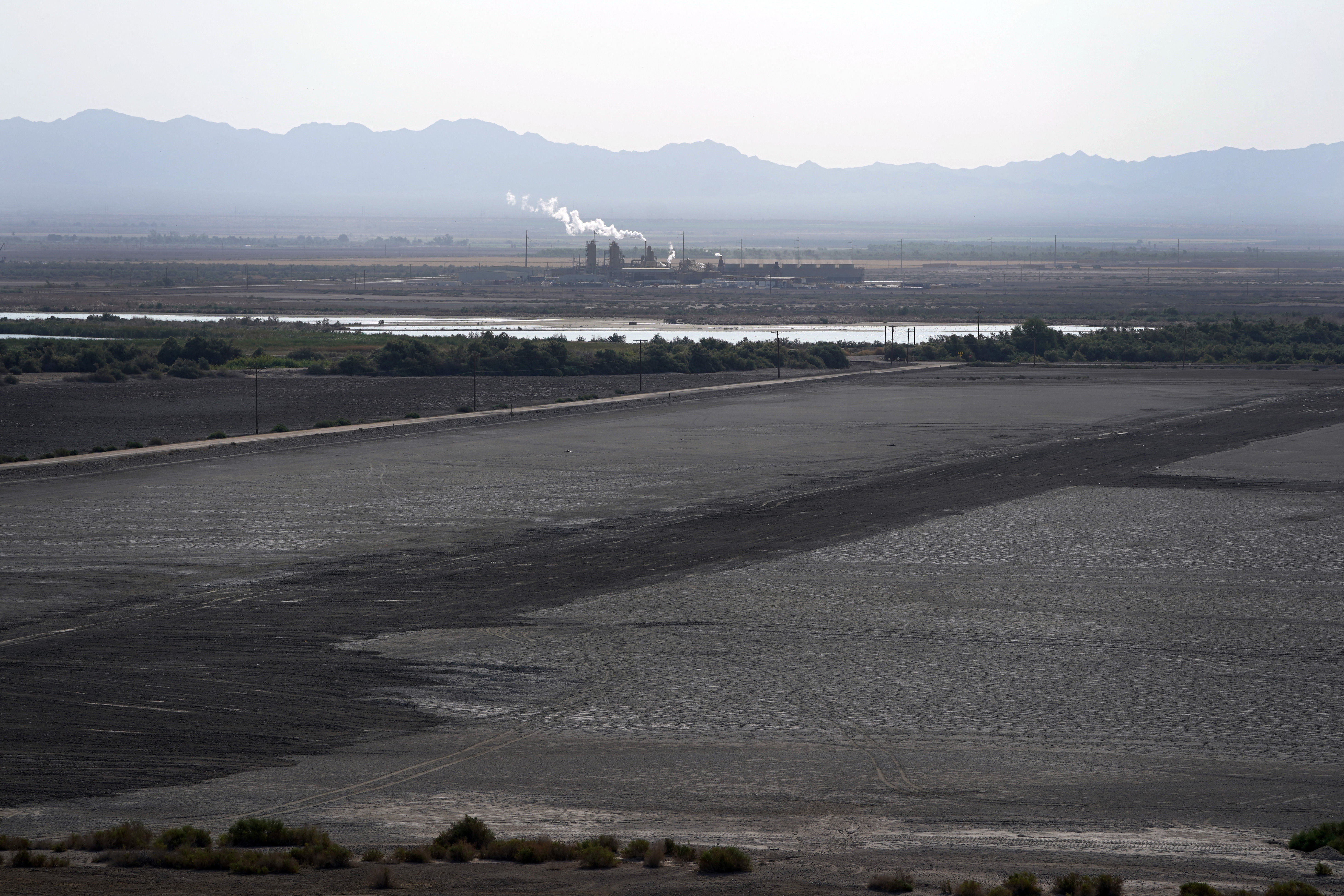A dried up portion of the Salton Sea stretches out with a geothermal power plant in the distance in Niland, Calif., July 15, 2021. Demand for electric vehicles has shifted investments into high gear to extract lithium from geothermal wastewater around the rapidly shrinking body of water. 