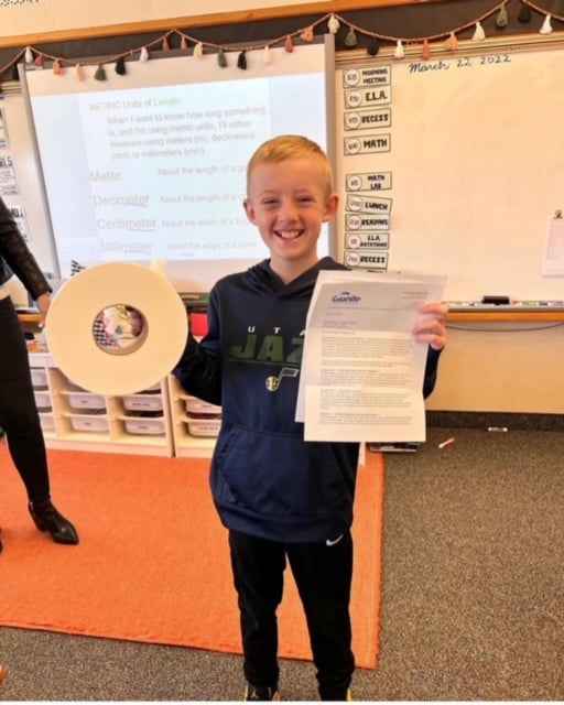 Jacob Paulson poses for a picture with an industrial-sized roll of two-ply toilet paper and a letter from a school district official.