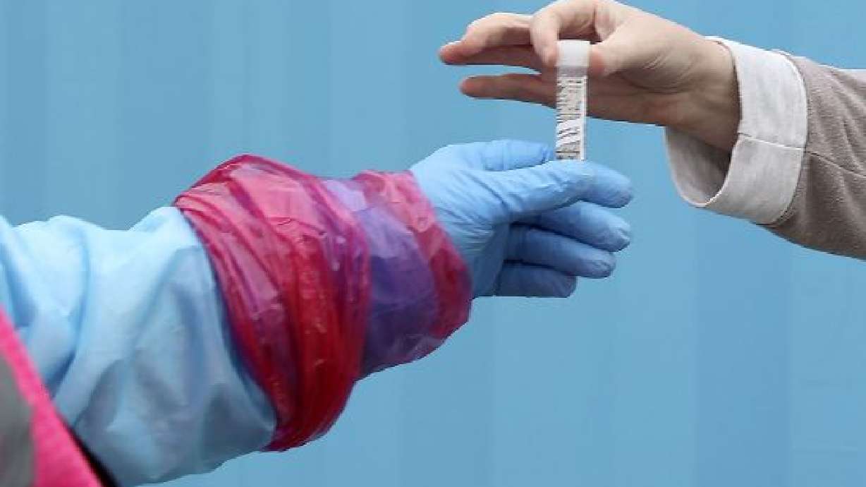 A woman hands her saliva sample to a worker at a COVID-19 testing site in Bountiful on Jan. 19.