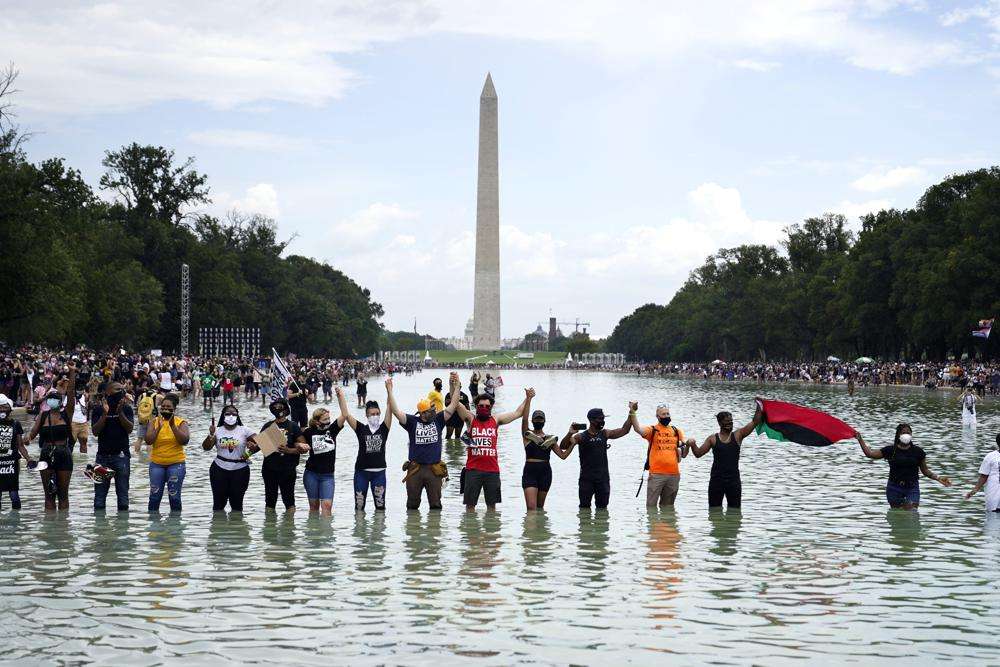 People join hands as they pose for a photo in the Reflecting Pool in the shadow of the Washington Monument as they attend the March on Washington, at the Lincoln Memorial in Washington, on the 57th anniversary of the Rev. Martin Luther King Jr.'s "I Have a Dream" speech on Aug. 28, 2020. California's first-in-the-nation task force on reparations is at a crossroads with members divided on which Black Americans should be eligible for compensation.