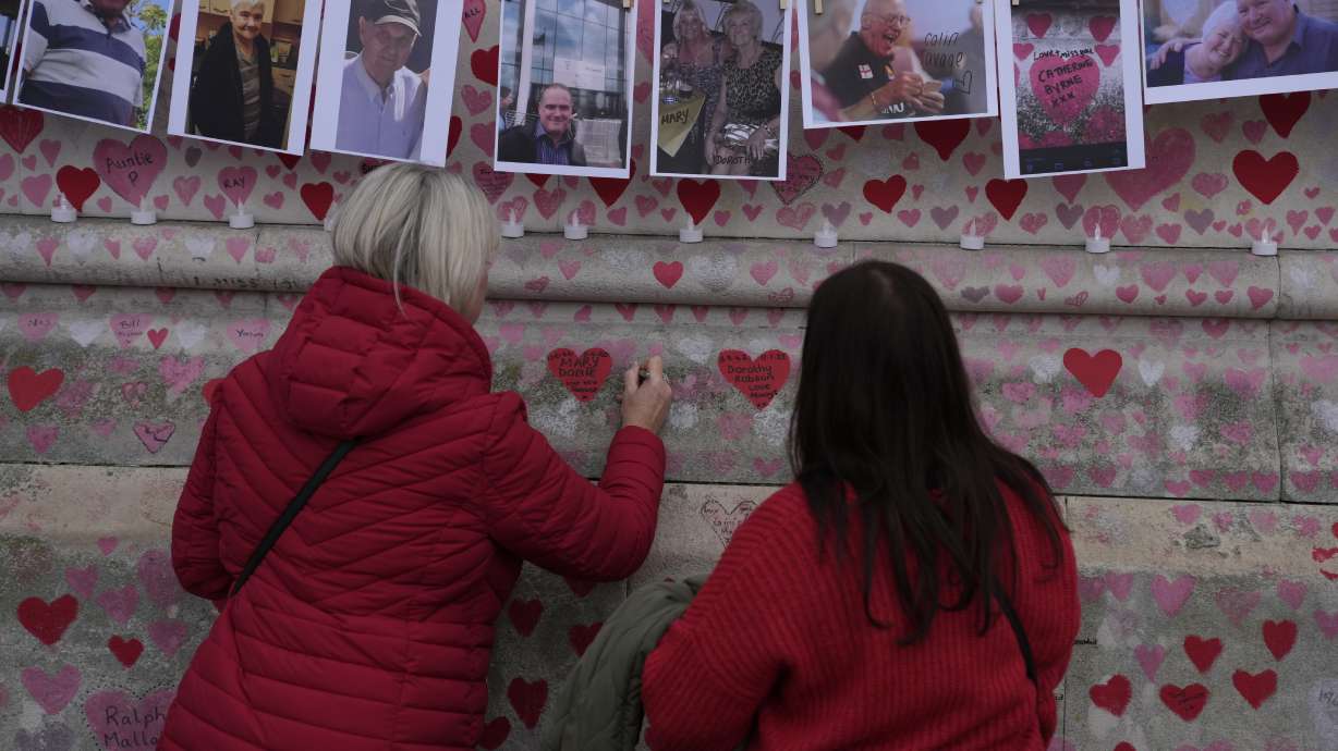 Family members write a message to two sisters who died of COVID on the National Covid Memorial wall in London, Tuesday. Latest figures from Britain's statistics agency show the prevalence of COVID-19 in the U.K. has reached record levels, with about 1 in 13 people estimated to be infected with the virus in the past week.