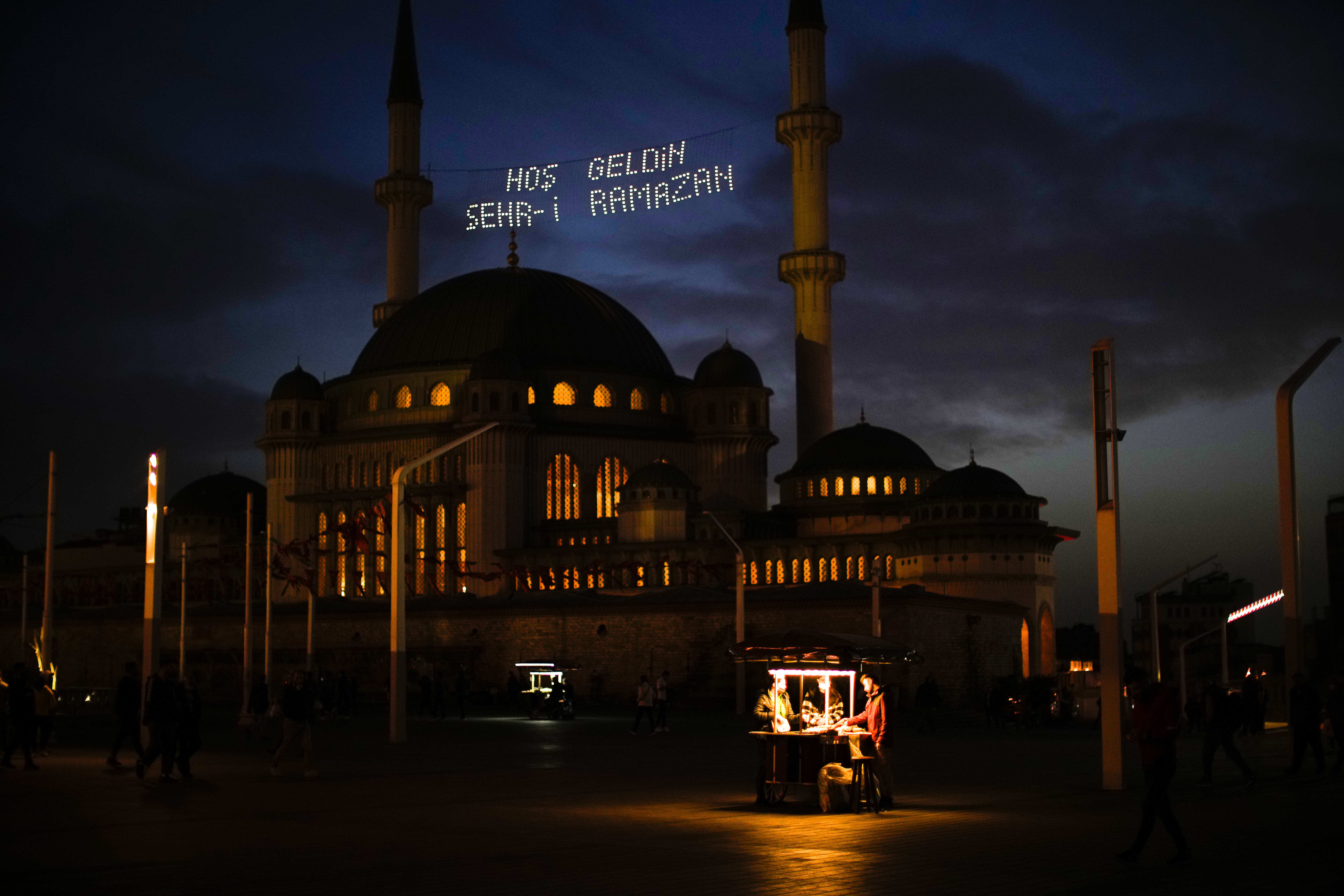 People buy roasted chestnuts next to Taksim mosque as the sun sets during the first day of the Muslim holy fasting month of Ramadan, in Istanbul, Turkey, Saturday. Lights on top read in Turkish: "Welcome Sehr-i Ramadan".