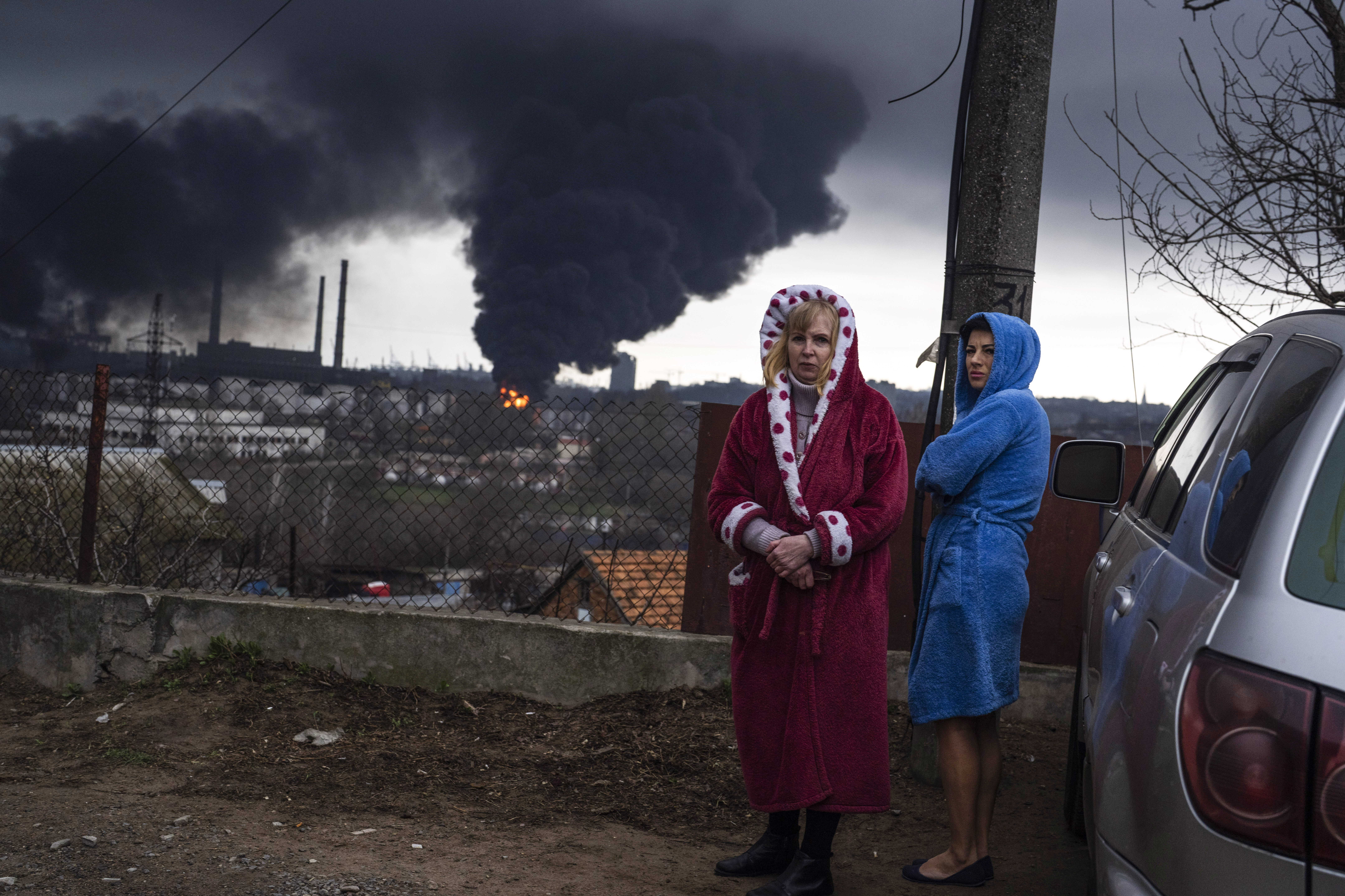 Women stay next to a car as smoke rises in the air in the background after shelling in Odesa, Ukraine, Sunday.