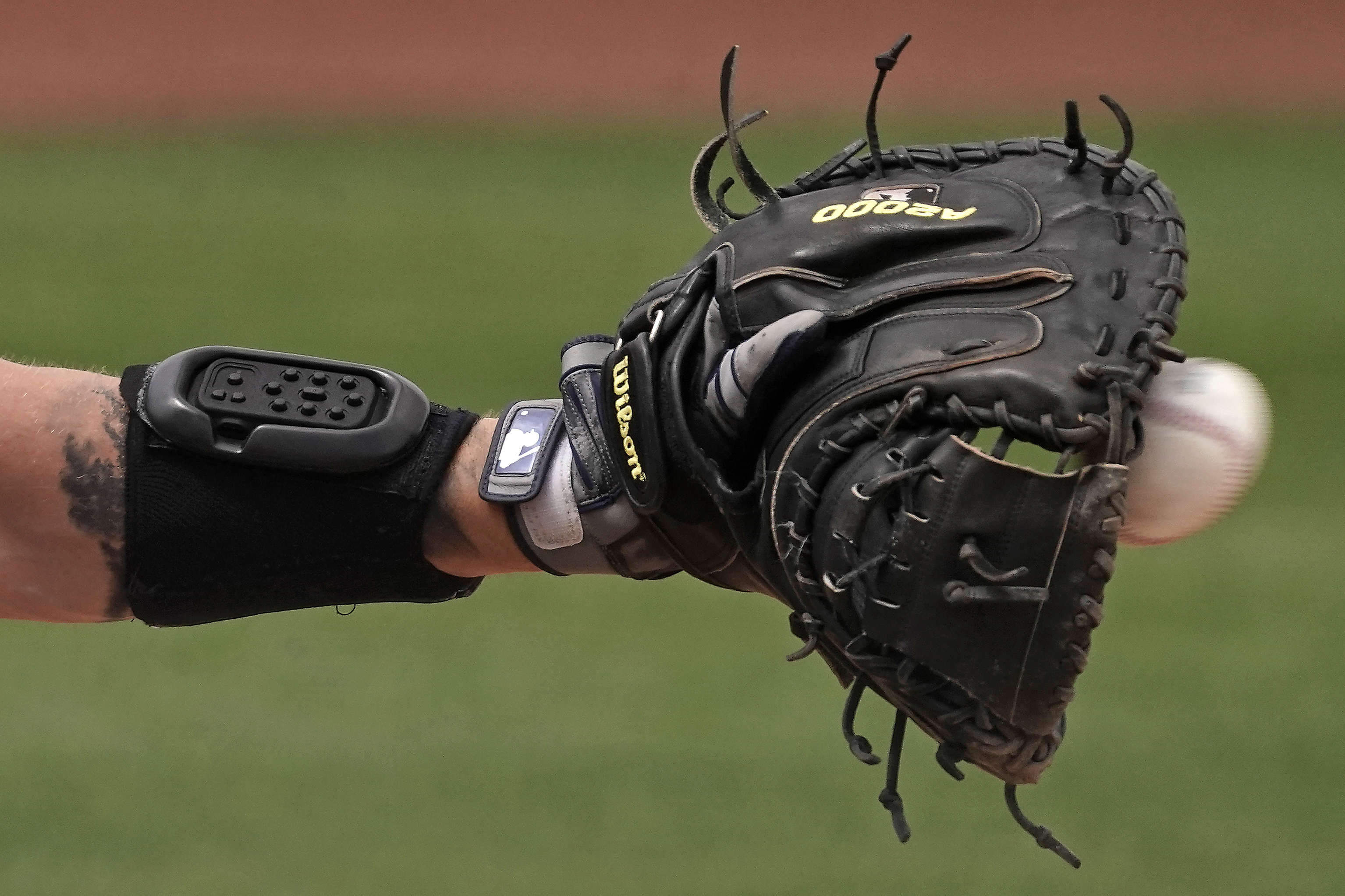 Seattle Mariners catcher Tom Murphy wears a wrist-worn device used to call pitches as he catches a ball during the sixth inning of a spring training baseball game against the Kansas City Royals, Tuesday, March 29, 2022, in Peoria, Ariz. The MLB is experimenting with the PitchCom system where the catcher enters information on a wrist band with nine buttons which is transmitted to the pitcher to call a pitch.