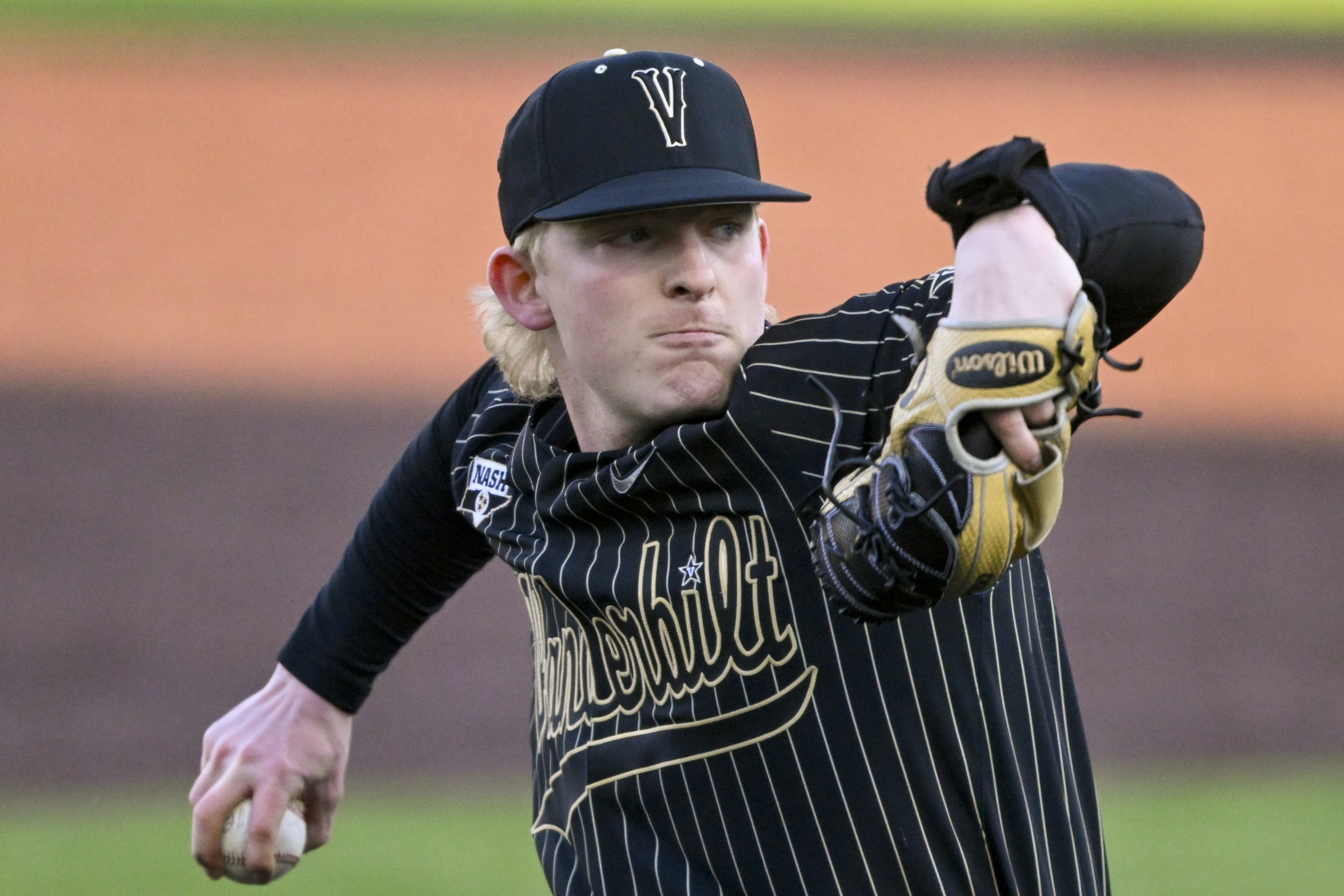 FILE - Vanderbilt pitcher Chris McElvain, wearing an electronic signal receiver on his left wrist, throws against Oklahoma State during an NCAA college baseball game, Feb. 18, 2022, in Nashville, Tenn. A growing number of college baseball teams are moving away from the tradition of catchers using their fingers and hands for pitch signs. The NCAA this year is allowing teams to have a coach in the dugout press into a keypad numbers corresponding to different pitch types and transmitting the information to a wristband worn by the pitcher.