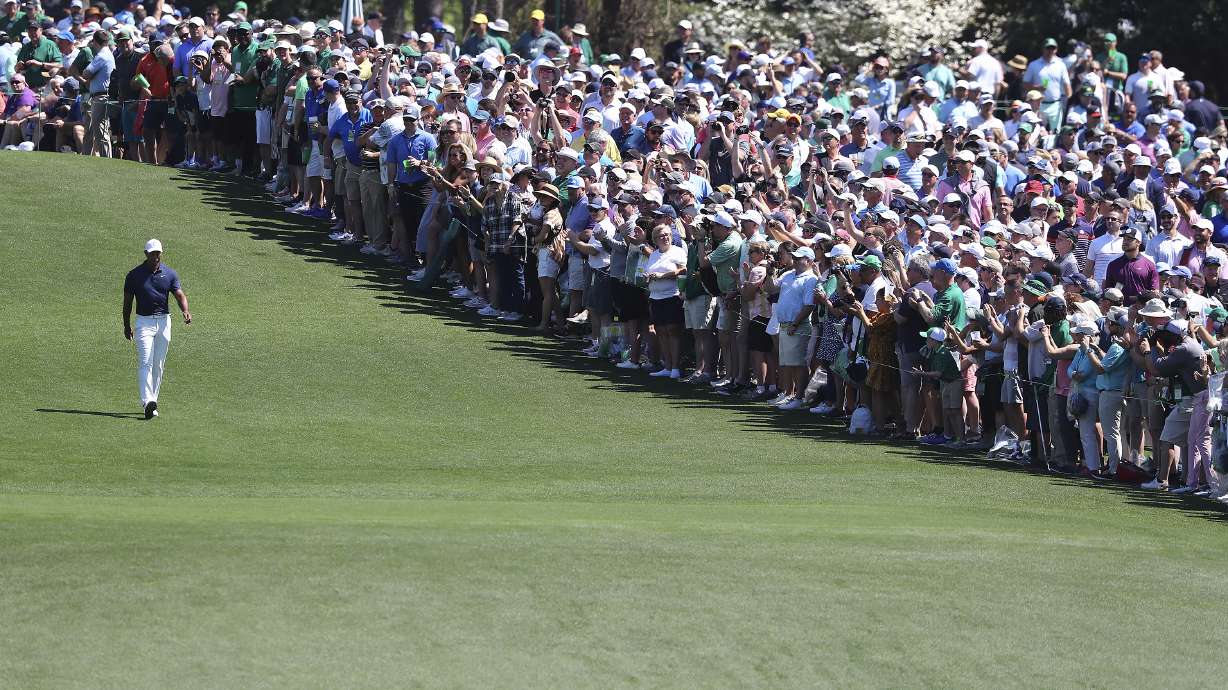 The giant gallery of patrons following five-time Masters champion Tiger Woods applaude as he walks down the first fairway after teeing off to begin his practice round for the Masters at Augusta National Golf Club in Augusta, Ga., Monday, April 4, 2022.