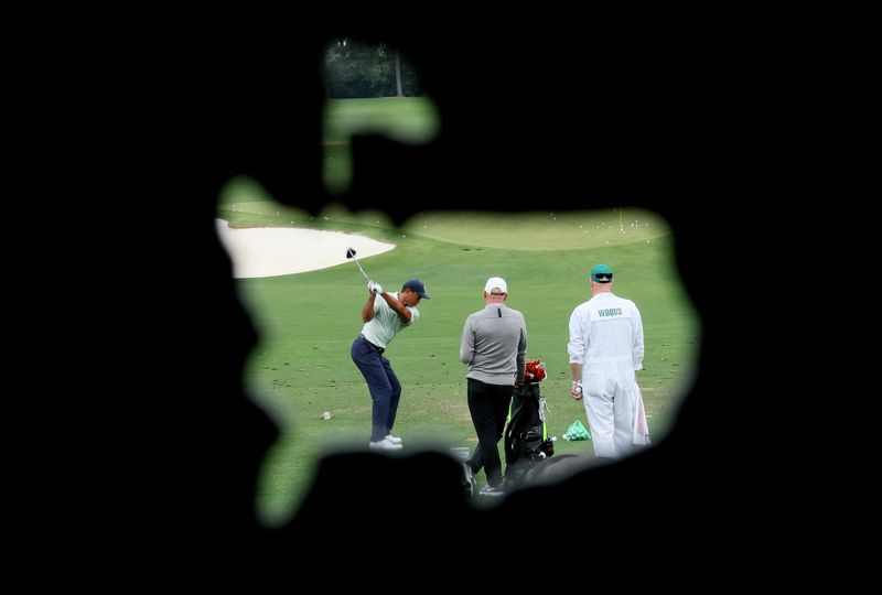 Golf - The Masters - Augusta National Golf Club - Augusta, Georgia, U.S. - April 5, 2022 Tiger Woods of the U.S. is seen through the logo of the Augusta National Golf Club hitting a shot on the practice tee