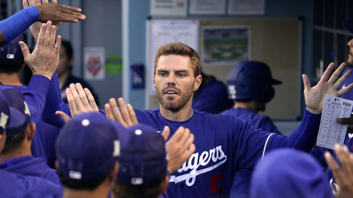 Los Angeles Dodgers' Freddie Freeman is congratulated by teammates in the dugout after scoring on a double by Trea Turner during the first inning of a spring training baseball game against the Los Angeles Angels Tuesday, in Los Angeles.