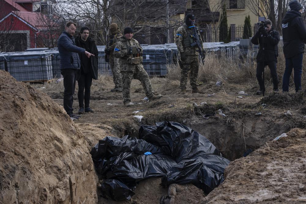 People stand next to a mass grave in Bucha, on the outskirts of Kyiv, Ukraine, Monday. Kremlin-backed media are denouncing atrocities in Bucha as an elaborate hoax.
