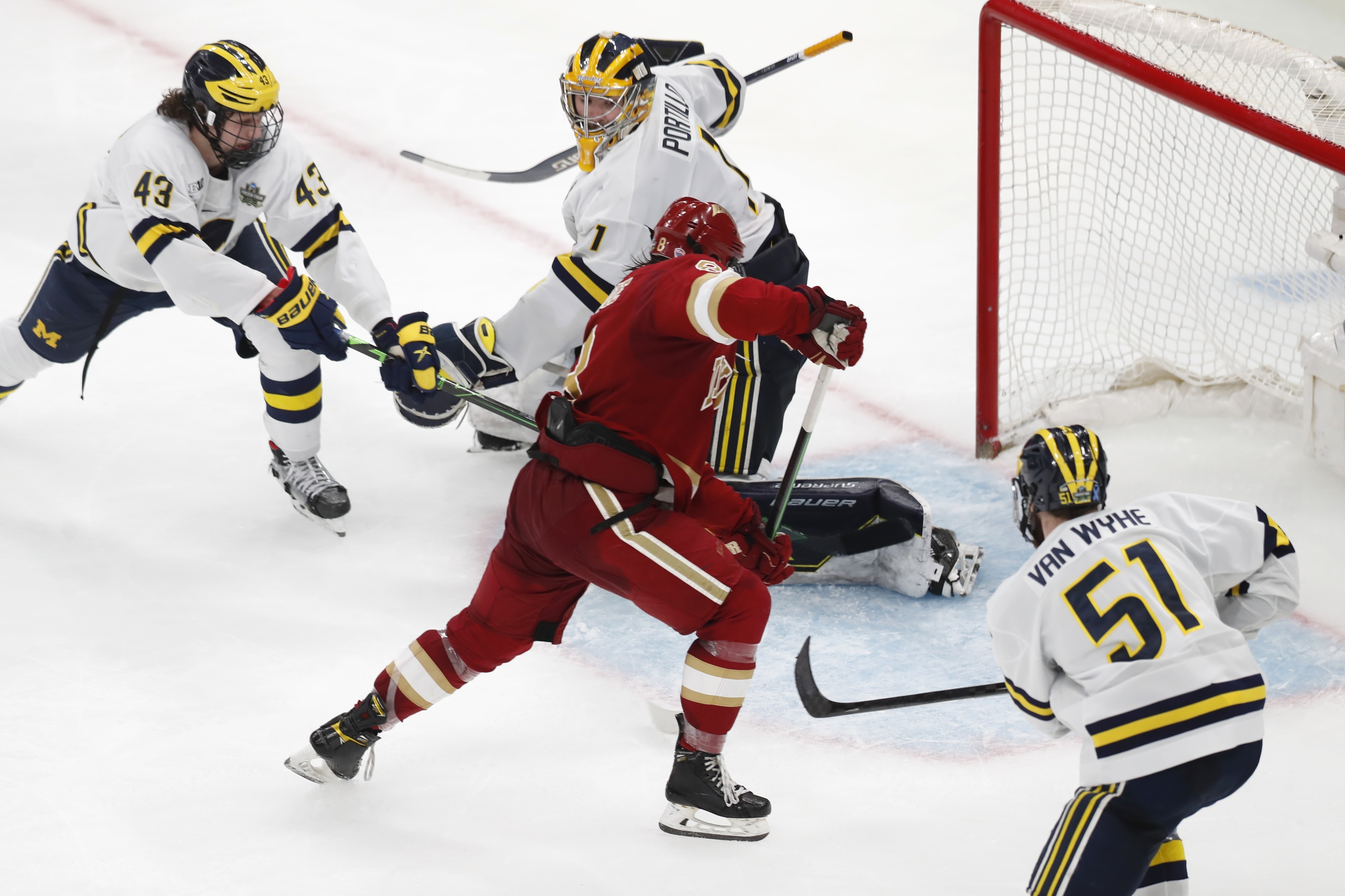 Denver's Carter Savoie (8) gathers the puck for the winning goal on Michigan's Erik Portillo (1) in overtime during an NCAA men's Frozen Four semifinal hockey game, Thursday, April 7, 2022, in Boston. 