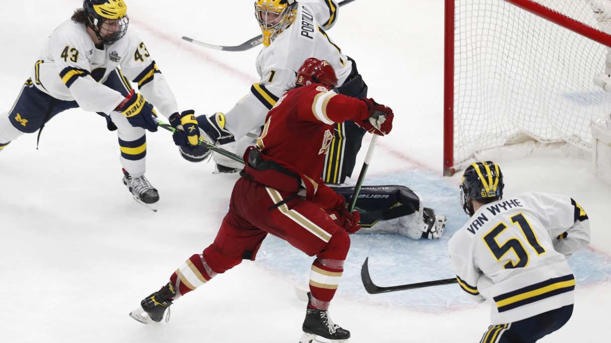 Denver's Carter Savoie (8) gathers the puck for the winning goal on Michigan's Erik Portillo (1) in overtime during an NCAA men's Frozen Four semifinal hockey game, Thursday, April 7, 2022, in Boston.