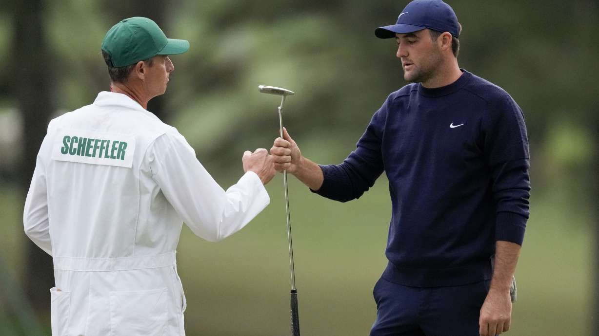 Scottie Scheffler bumps fists with his caddie, Ted Scott, after putting in on the 18th green during the second round at the Masters golf tournament Friday, April 8, 2022, in Augusta, Ga.