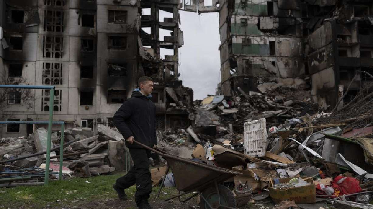 A young man pushes a wheelbarrow in front of a destroyed apartment building in the town of Borodyanka, Ukraine, on Sunday. Shocking atrocities in Ukraine, allegedly at the hands of Russian forces, have amplified calls to pursue war crimes charges against Russian President Vladimir Putin.