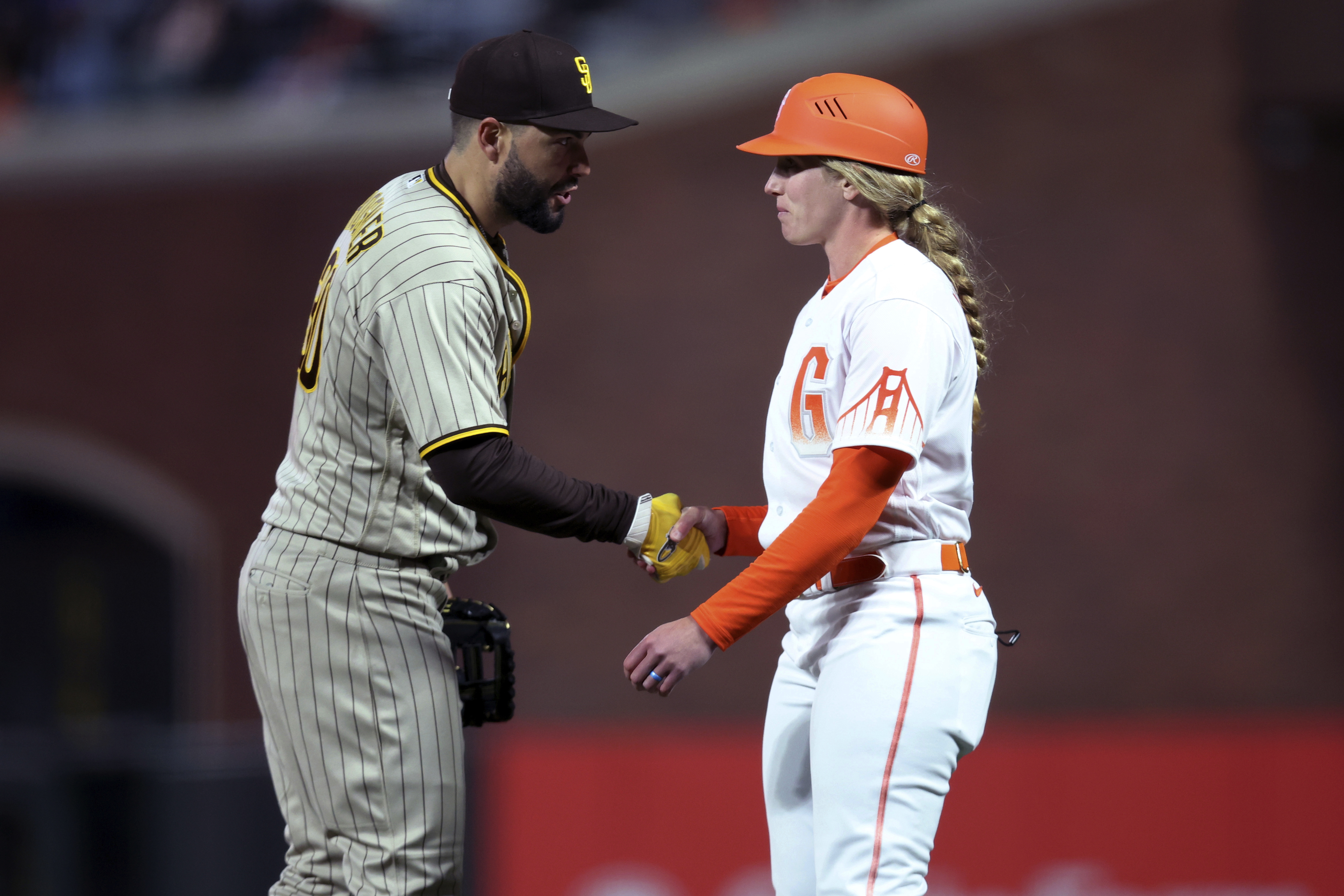 San Diego Padres first baseman Eric Hosmer, left, shakes hands with San Francisco Giants first base coach Alyssa Nakken during the third inning of a baseball game in San Francisco, Tuesday, April 12, 2022. 